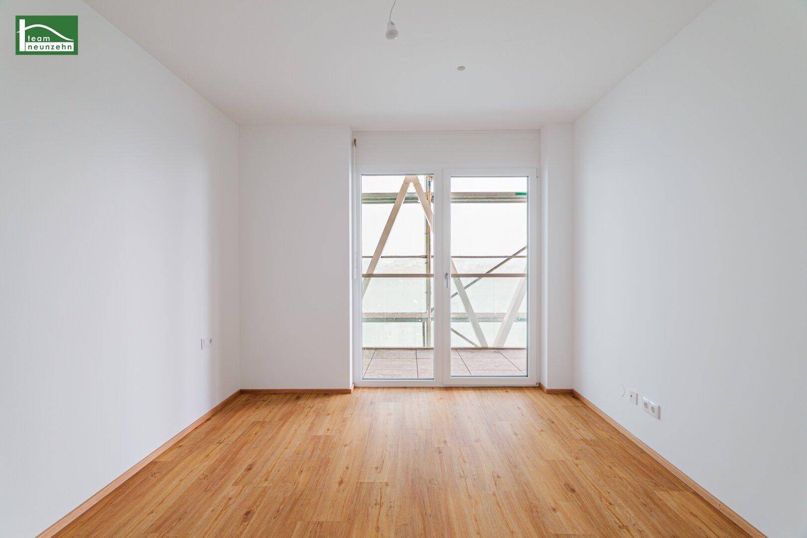 Geräumiges, leeres Zimmer mit hellem Holzboden und Balkonzugang, ideal als Schlafzimmer.