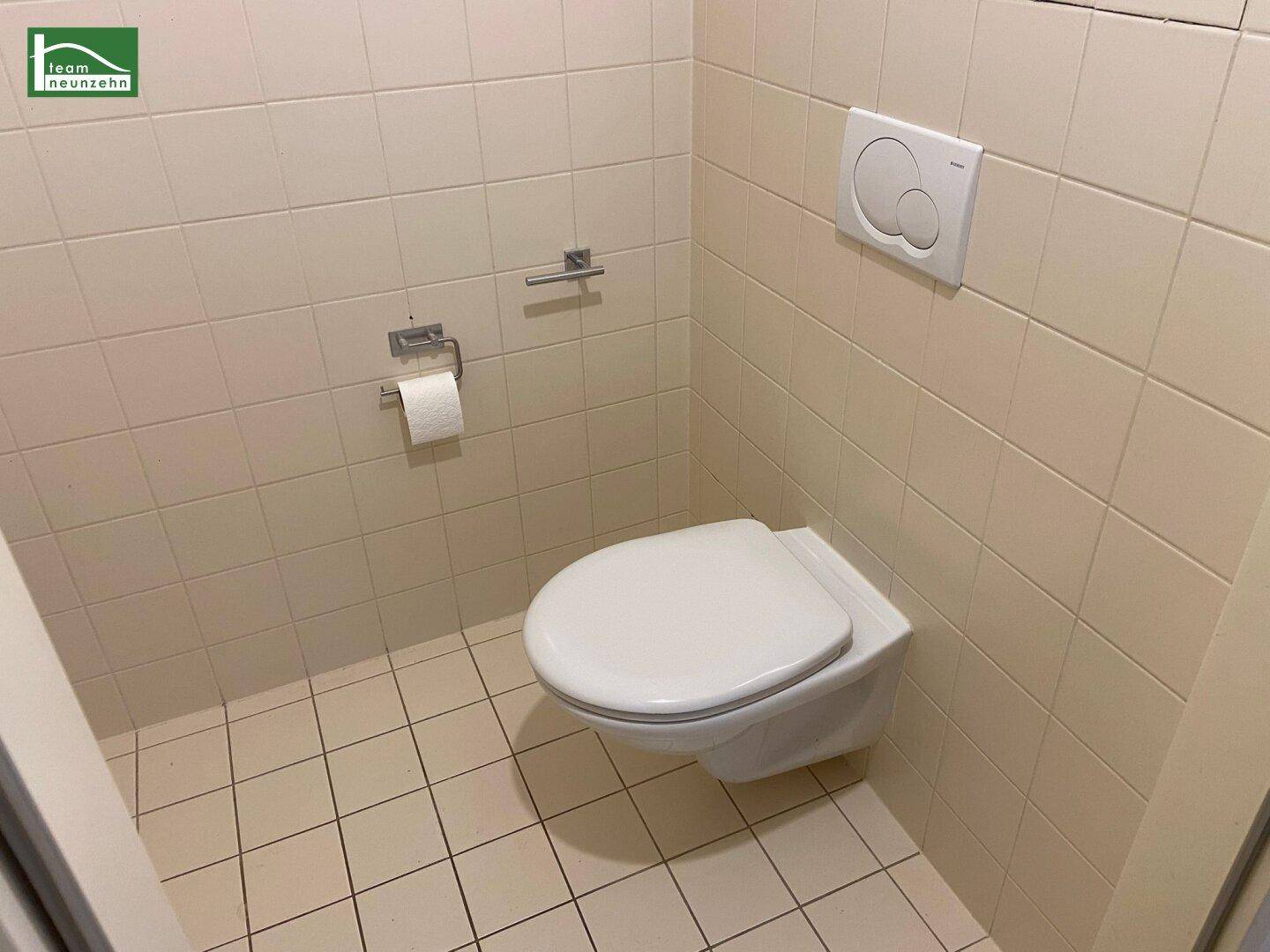 Separate Toilette mit wandhängendem WC und beigefarbenen Fliesen an Wänden und Boden.