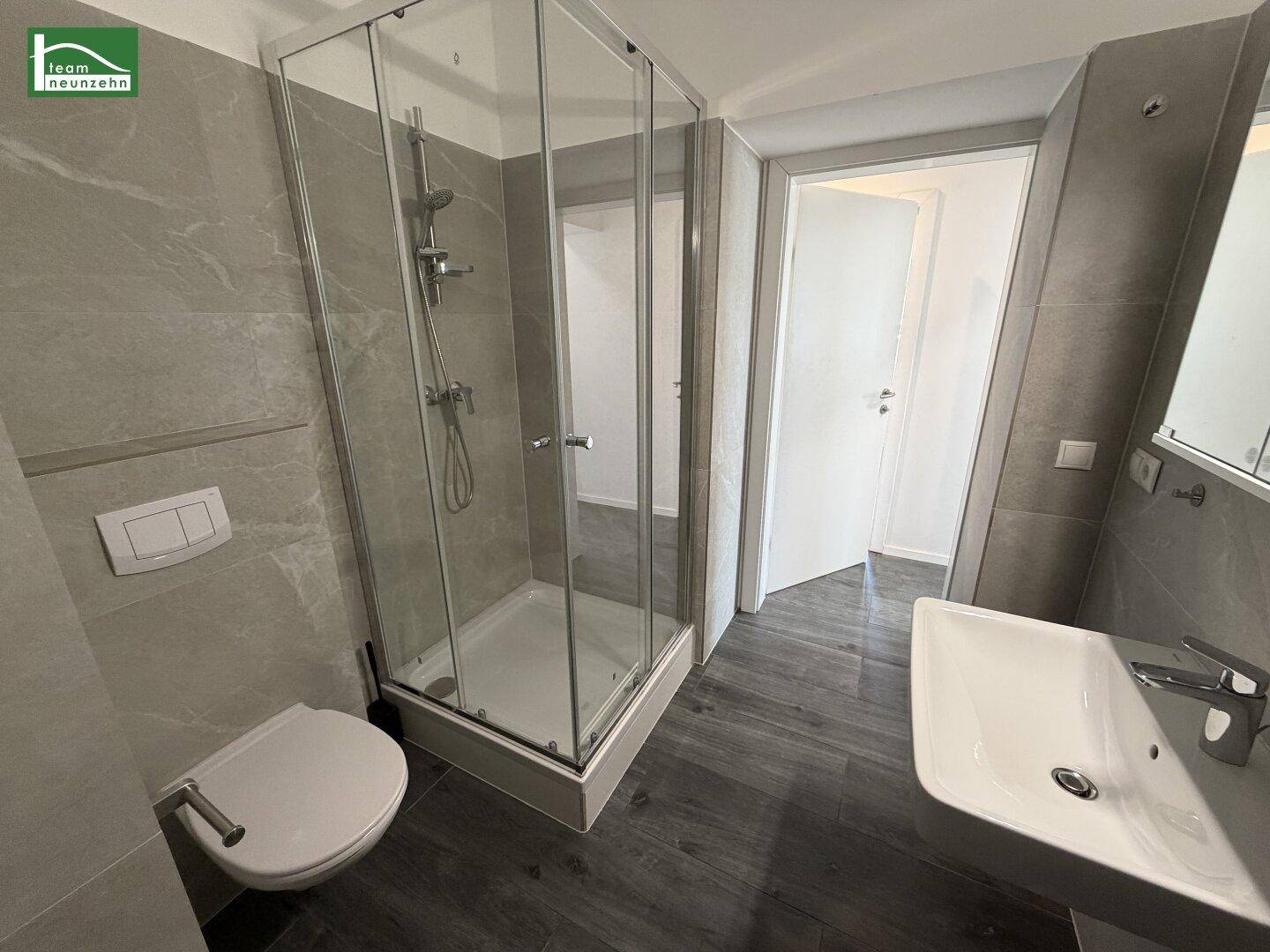 Zeitgemäßes Badezimmer mit Duschkabine, Waschbecken und WC, ausgestattet mit grauen Wandfliesen.
