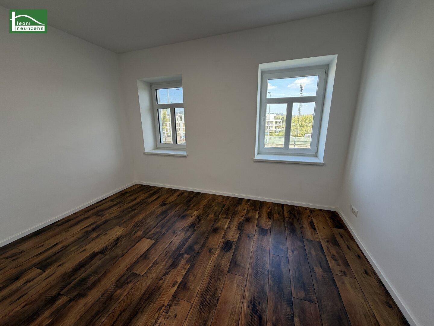 Helles Schlafzimmer mit Laminatboden und zwei Fenstern, bietet einen angenehmen Wohnkomfort.