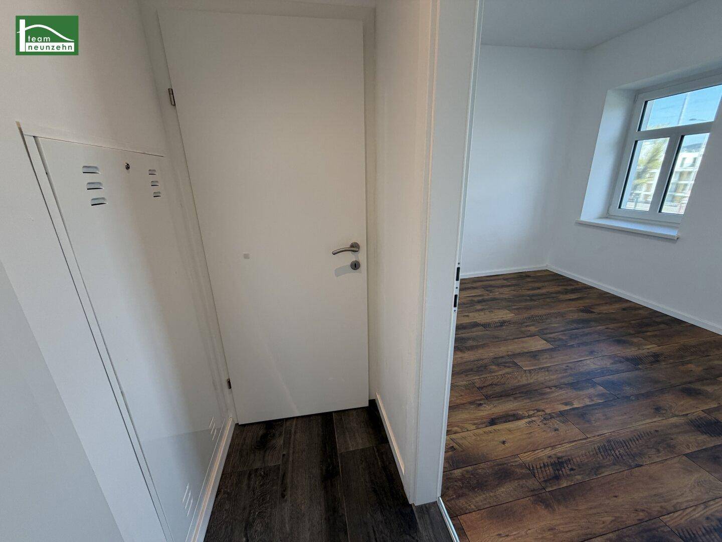 Flur mit dunklem Boden, weiß gestrichenen Wänden und Zugang zu einem angrenzenden Wohnraum.