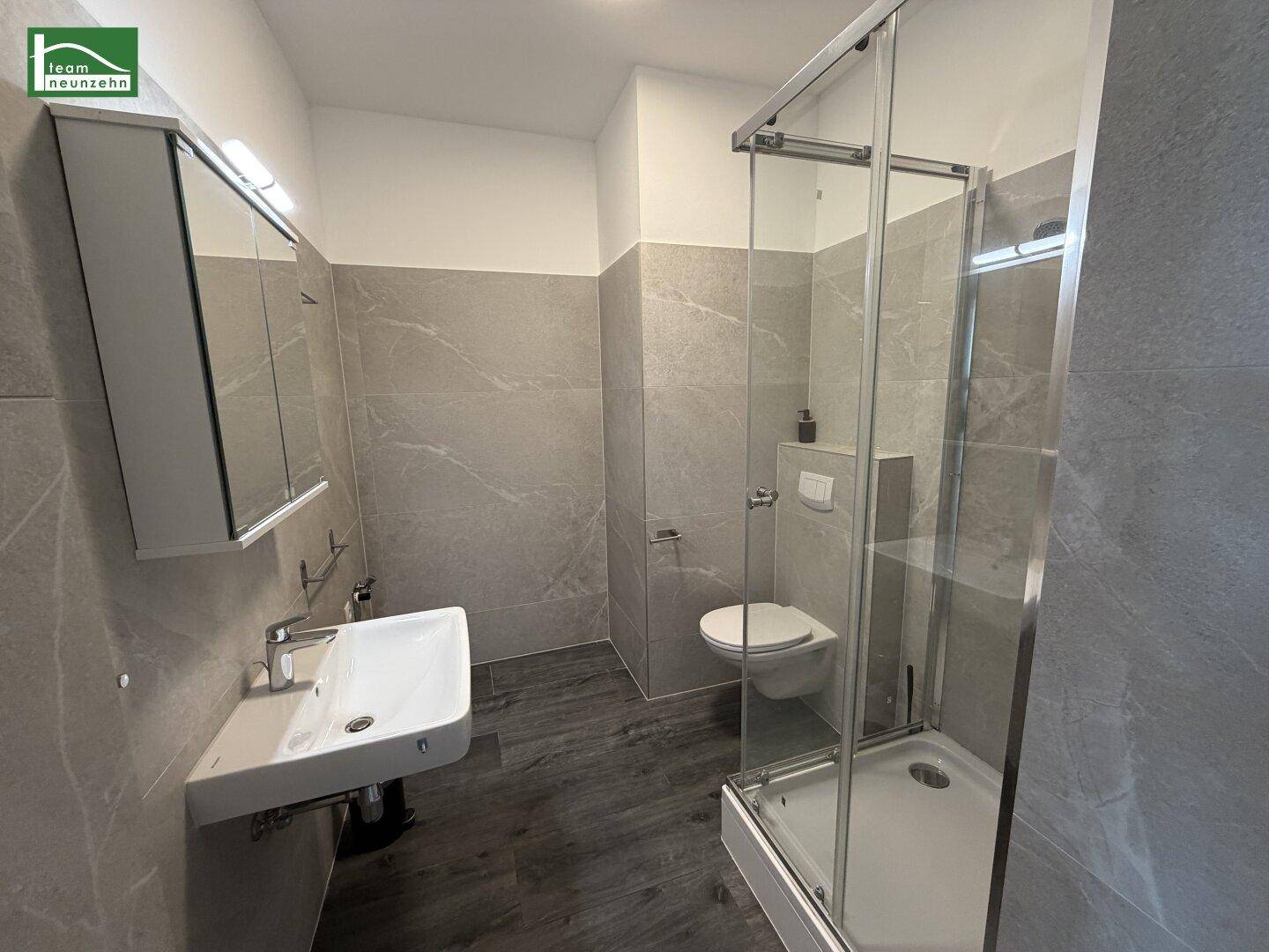 Modernes Badezimmer mit Duschkabine, Waschbecken und WC, in hellen Grautönen gehalten.