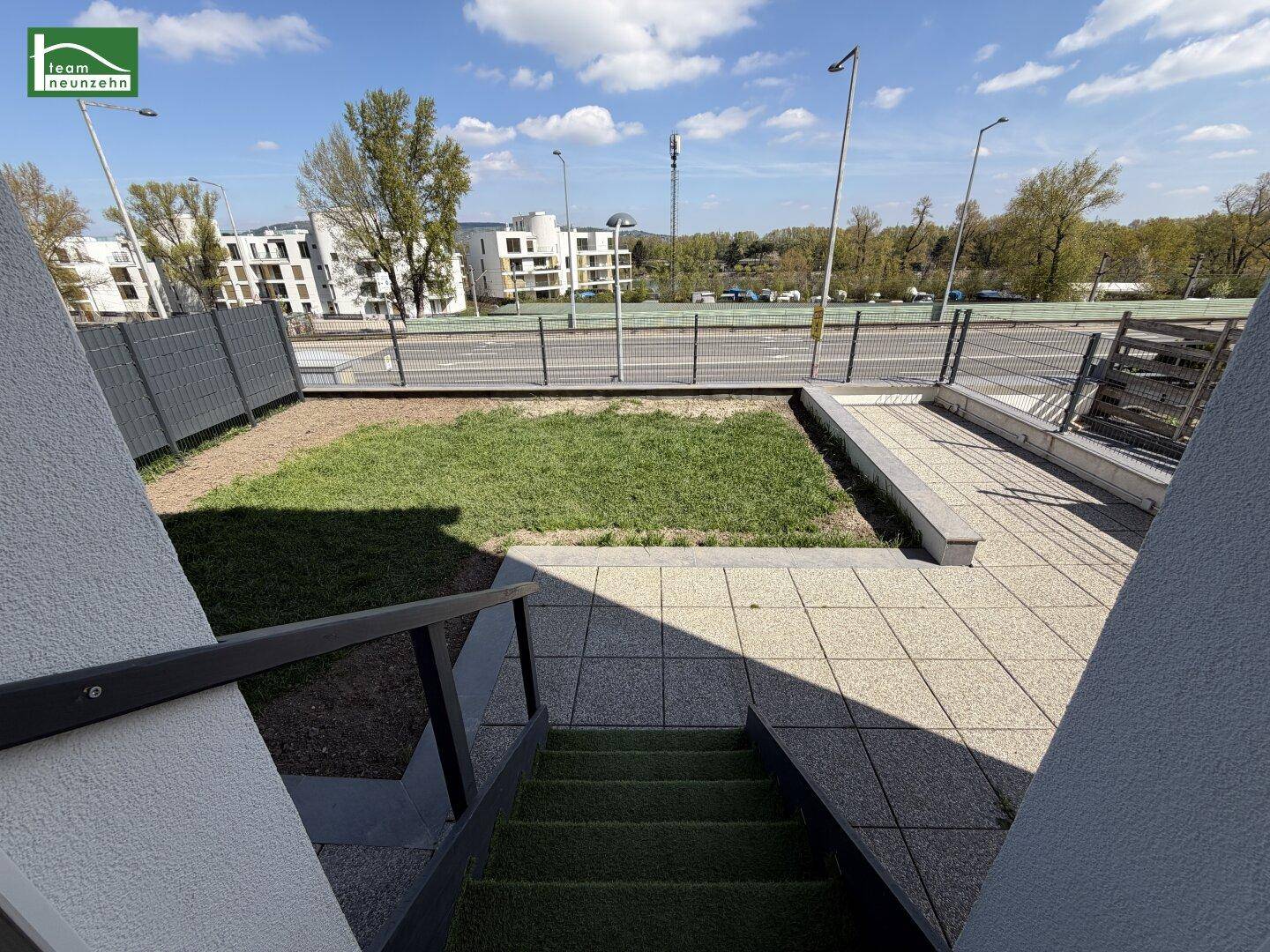 Außenterrasse mit Treppenzugang und kleiner Rasenfläche, umgeben von einer modernen Bebauung.