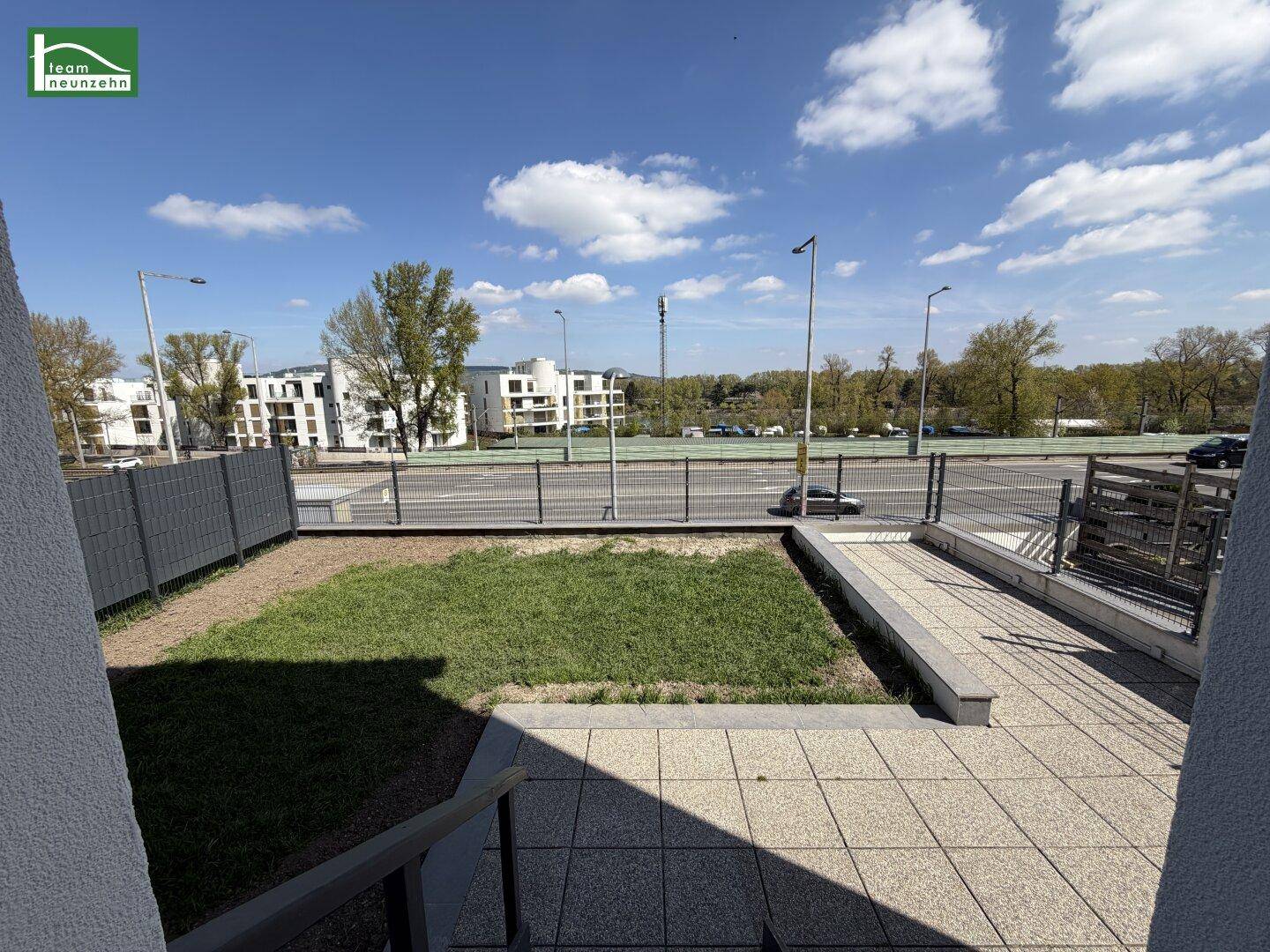 Außenterrasse mit Treppenzugang und kleiner Rasenfläche, umgeben von einer modernen Bebauung.