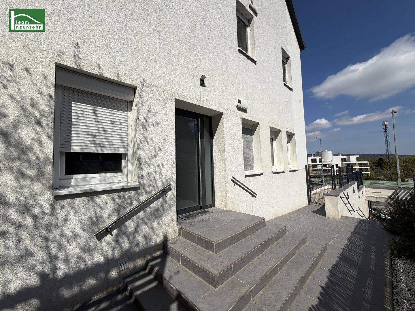 Gebäudeeingang mit Steintreppe und Handlauf, umgeben von einer modernen Fassade.