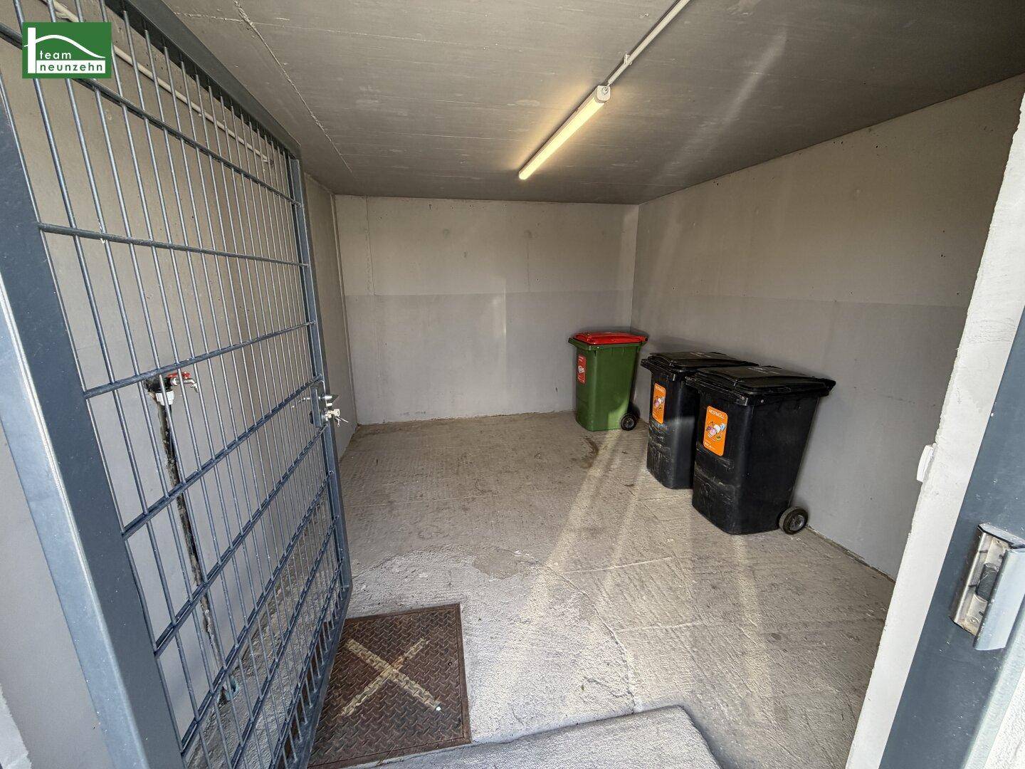 Geräumiger Abstellraum mit Betonboden und Mülltonnen, ideal für Lagerzwecke.
