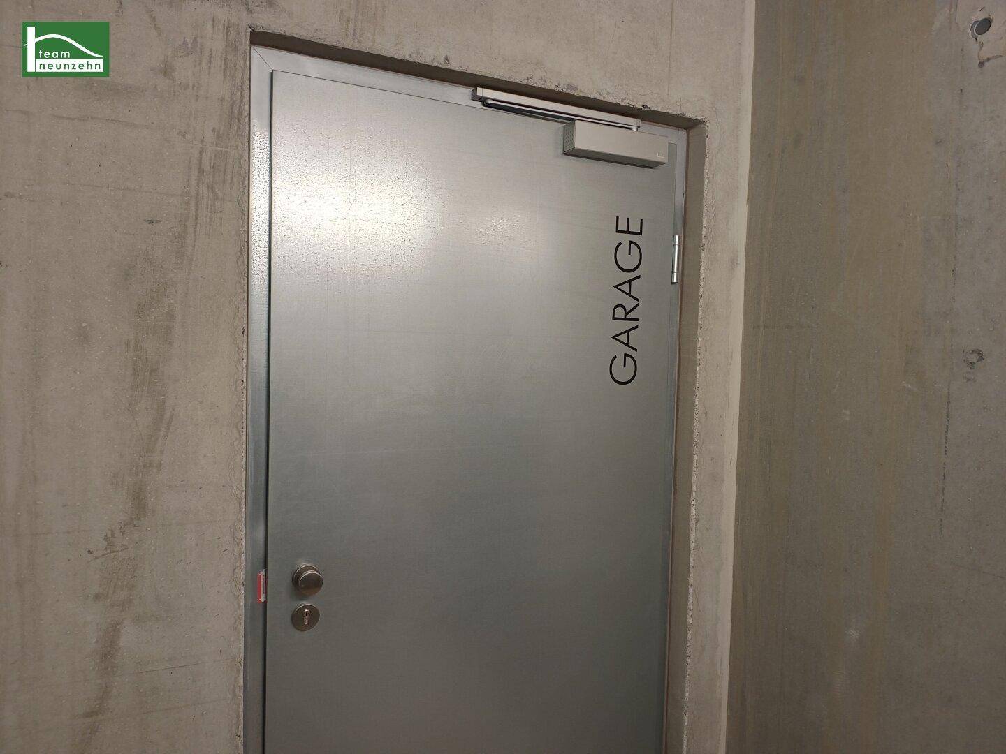 Eine robuste Metalltür mit der Aufschrift "GARAGE" in einer Betonwand, Zugang zur Tiefgarage.