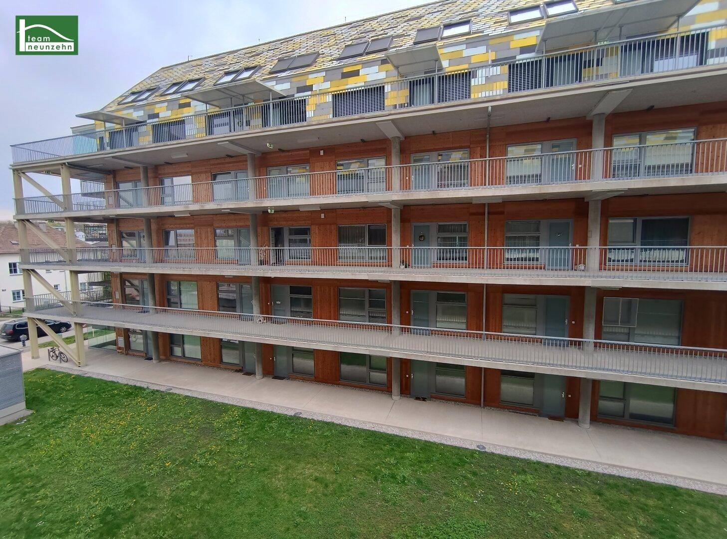 Moderne Wohnanlage mit Holzfassade, mehreren Balkonen und einer gepflegten Grünfläche davor.