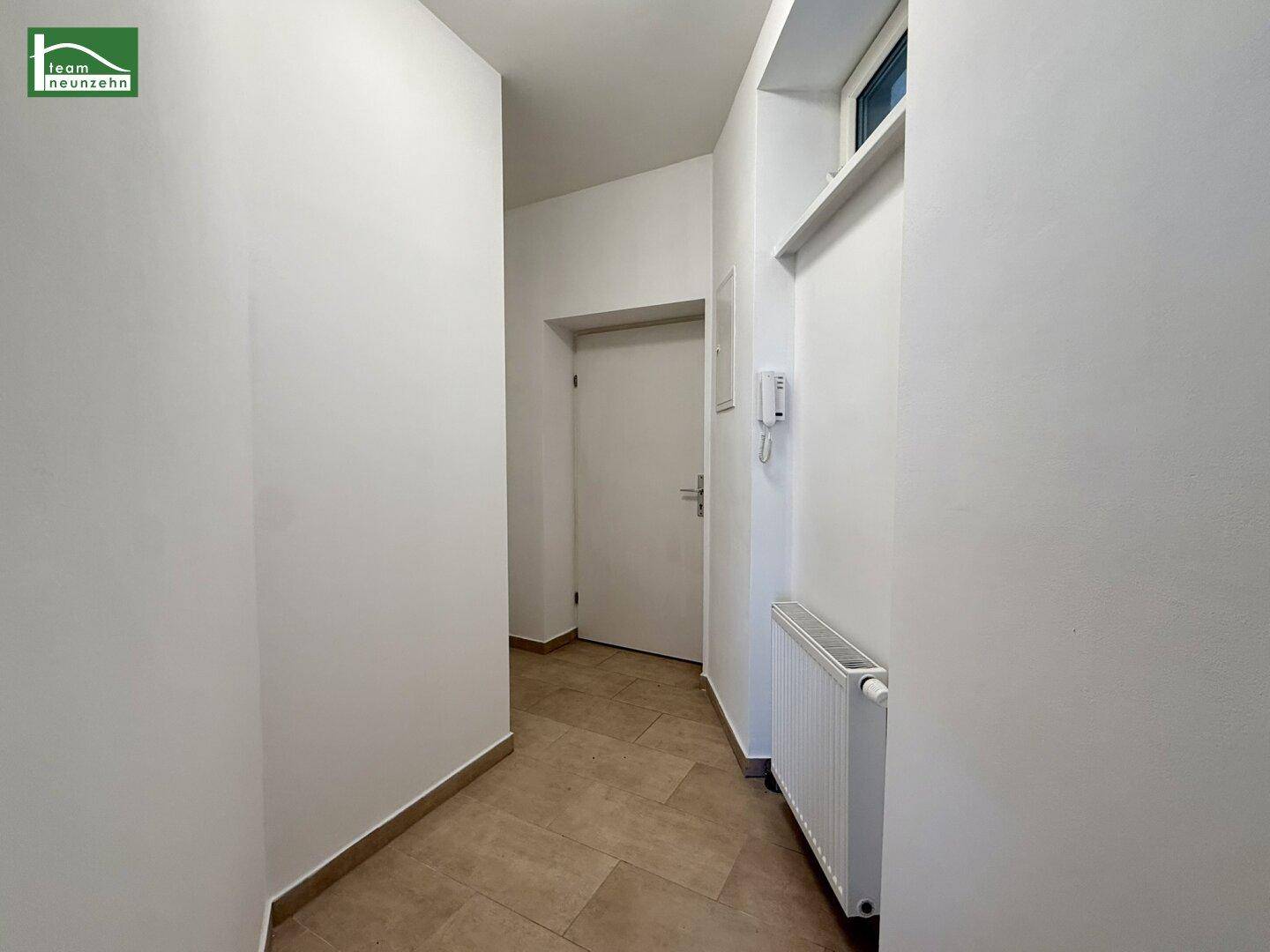 Schmaler Flur mit hellen Fliesen, Gegensprechanlage und Zugang zu weiteren Räumen.