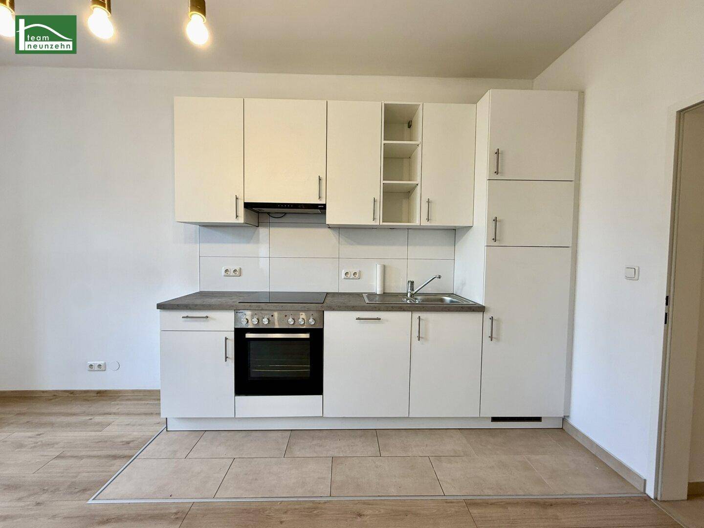 Moderne weiße Küchenzeile mit integriertem Backofen, Induktionskochfeld und Spüle.