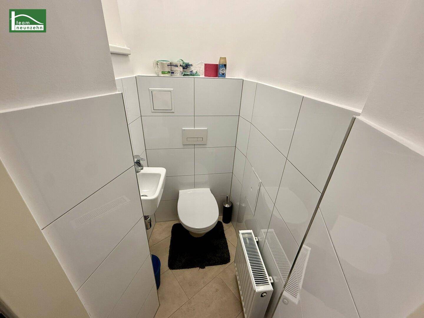 Separates Gäste-WC mit wandhängendem WC, kleinem Waschbecken und weißen Fliesen.
