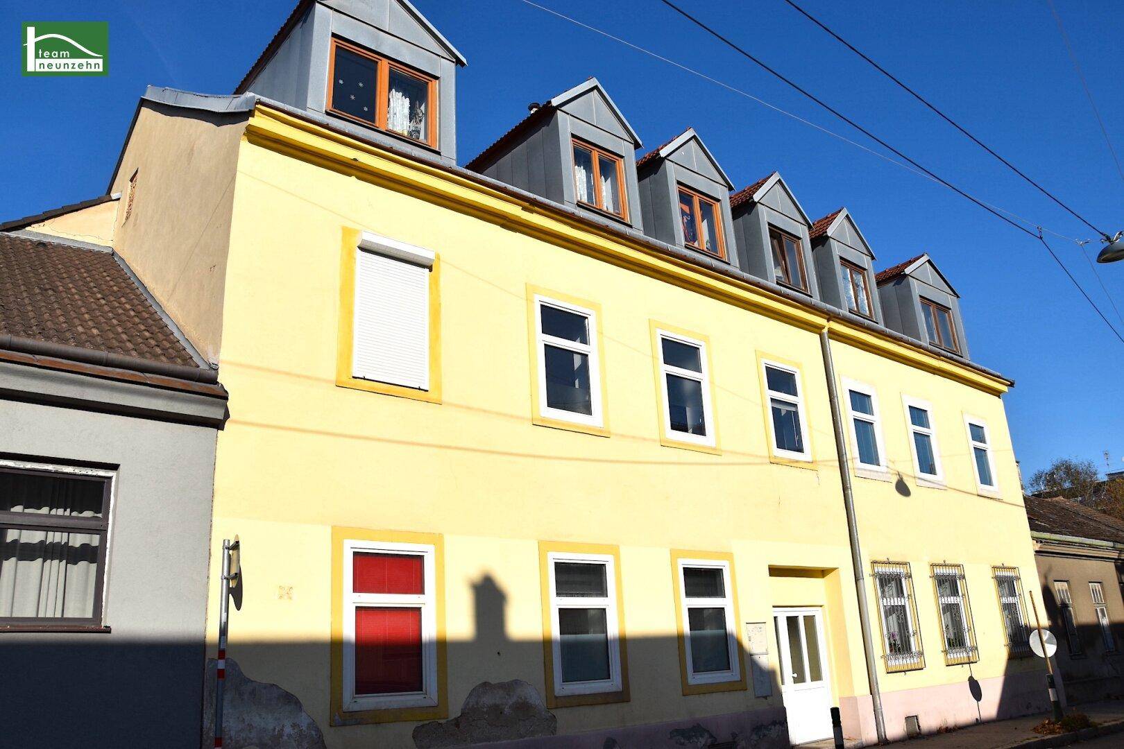 Gelbe Fassade eines Mehrfamilienhauses mit mehreren Dachgauben und weißen Fenstern.