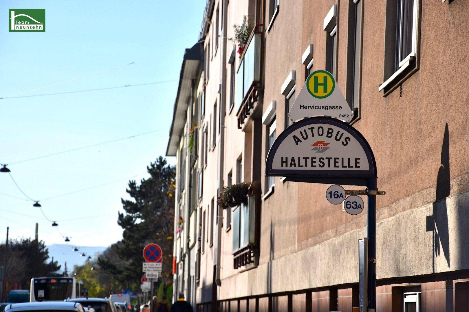 Außenansicht eines Gebäudes an einer Straße mit Bushaltestelle und klarem Himmel.