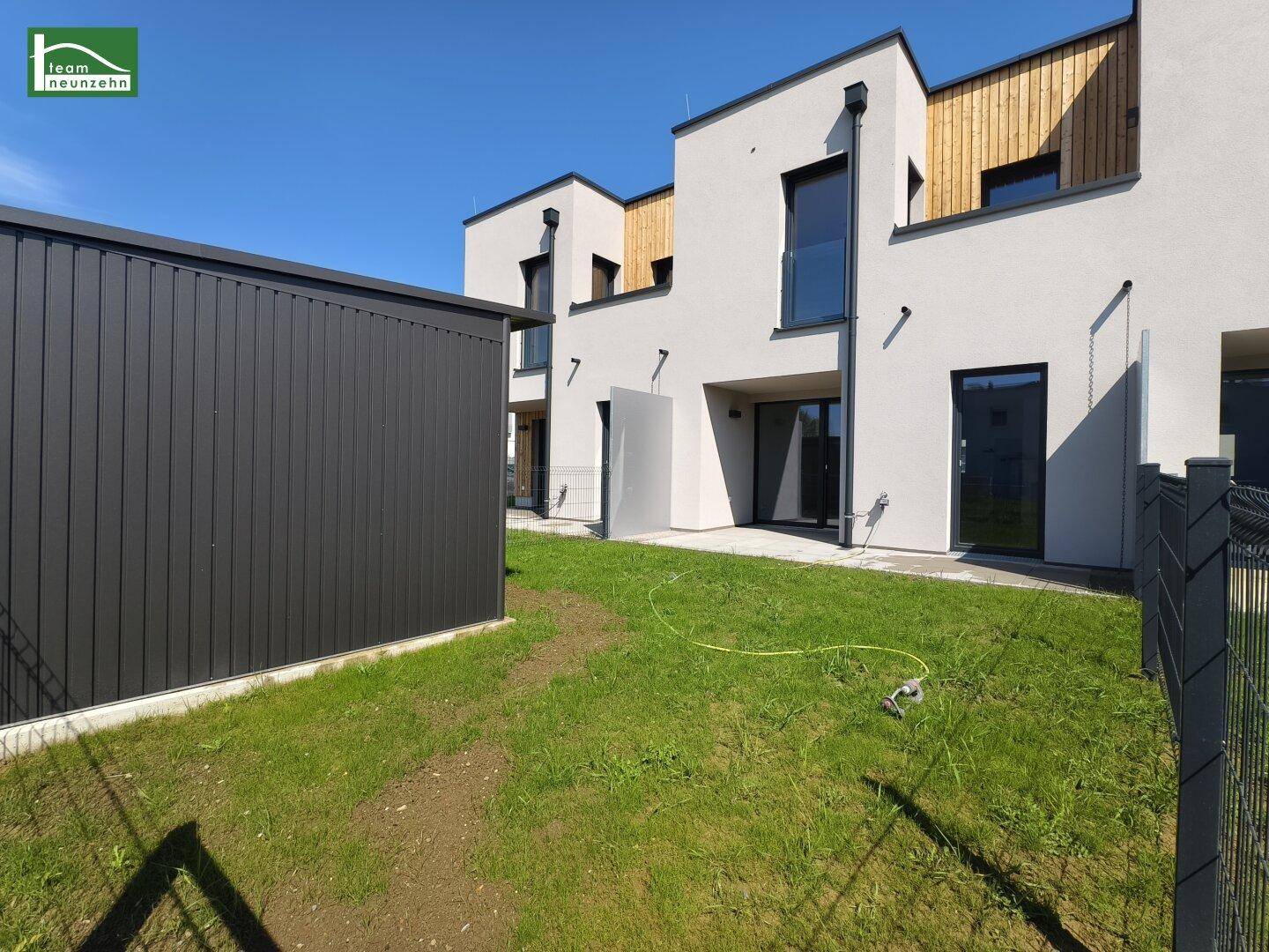 Moderne Reihenhäuser mit privatem Gartenbereich und einem praktischen Geräteschuppen unter blauem Himmel.