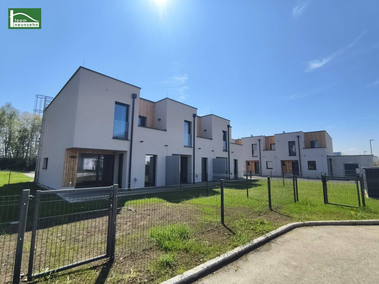 Reihenhäuser in moderner Architektur mit großen Fenstern und gepflegten Außenbereichen unter strahlendem Sonnenschein.