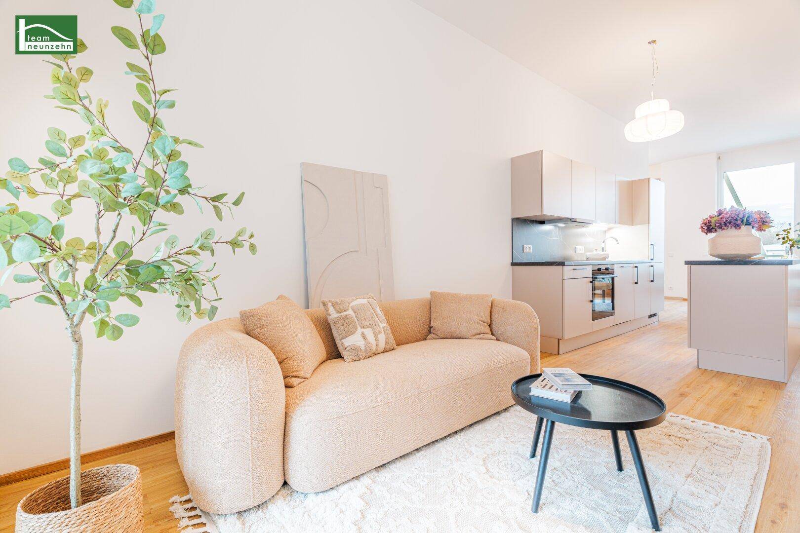 Gemütlicher Wohnbereich mit beigem Sofa, Couchtisch und offener Küche im Hintergrund.