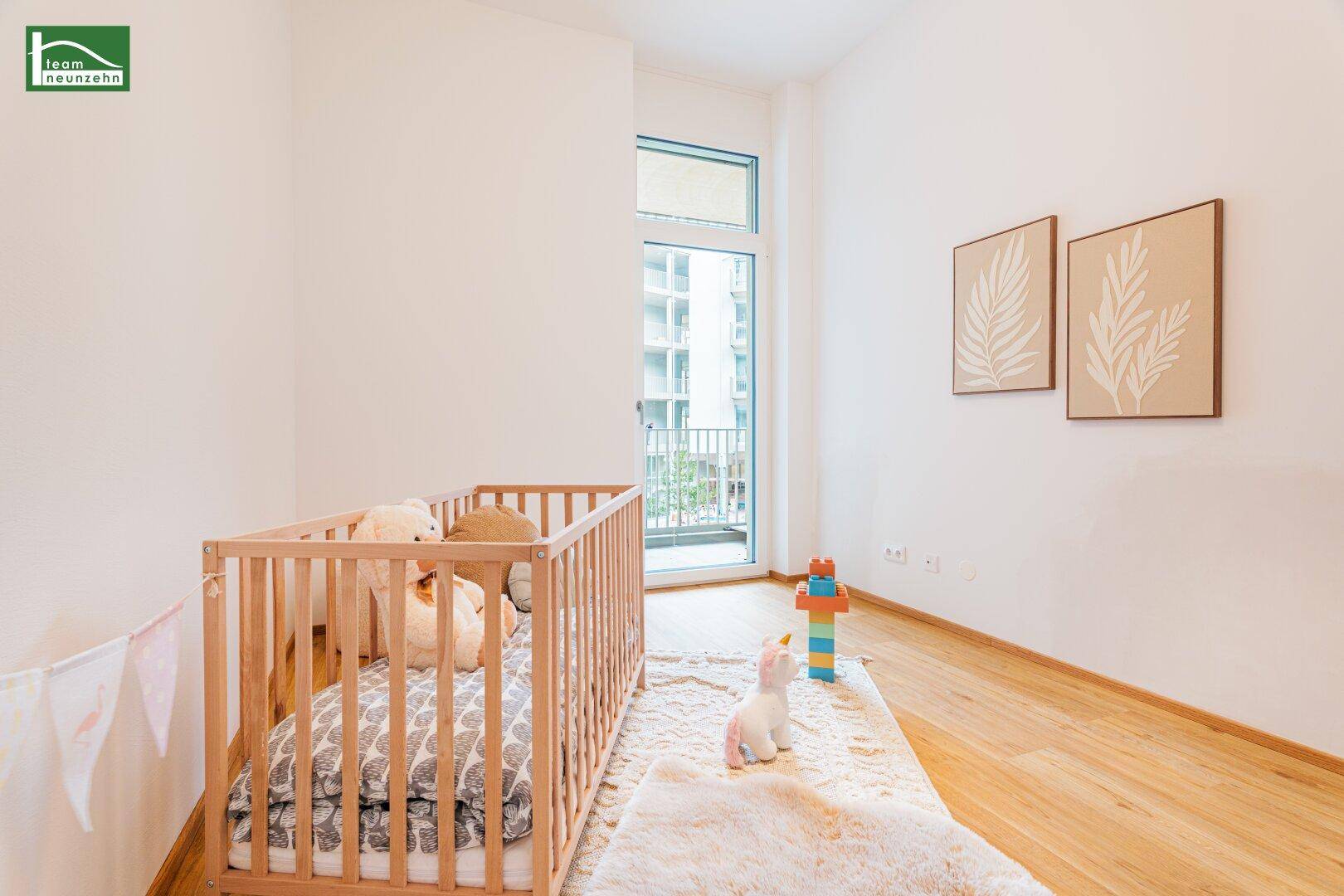 Helles Kinderzimmer mit Babybett, Holzboden und einem Fenster mit Blick auf die Umgebung.