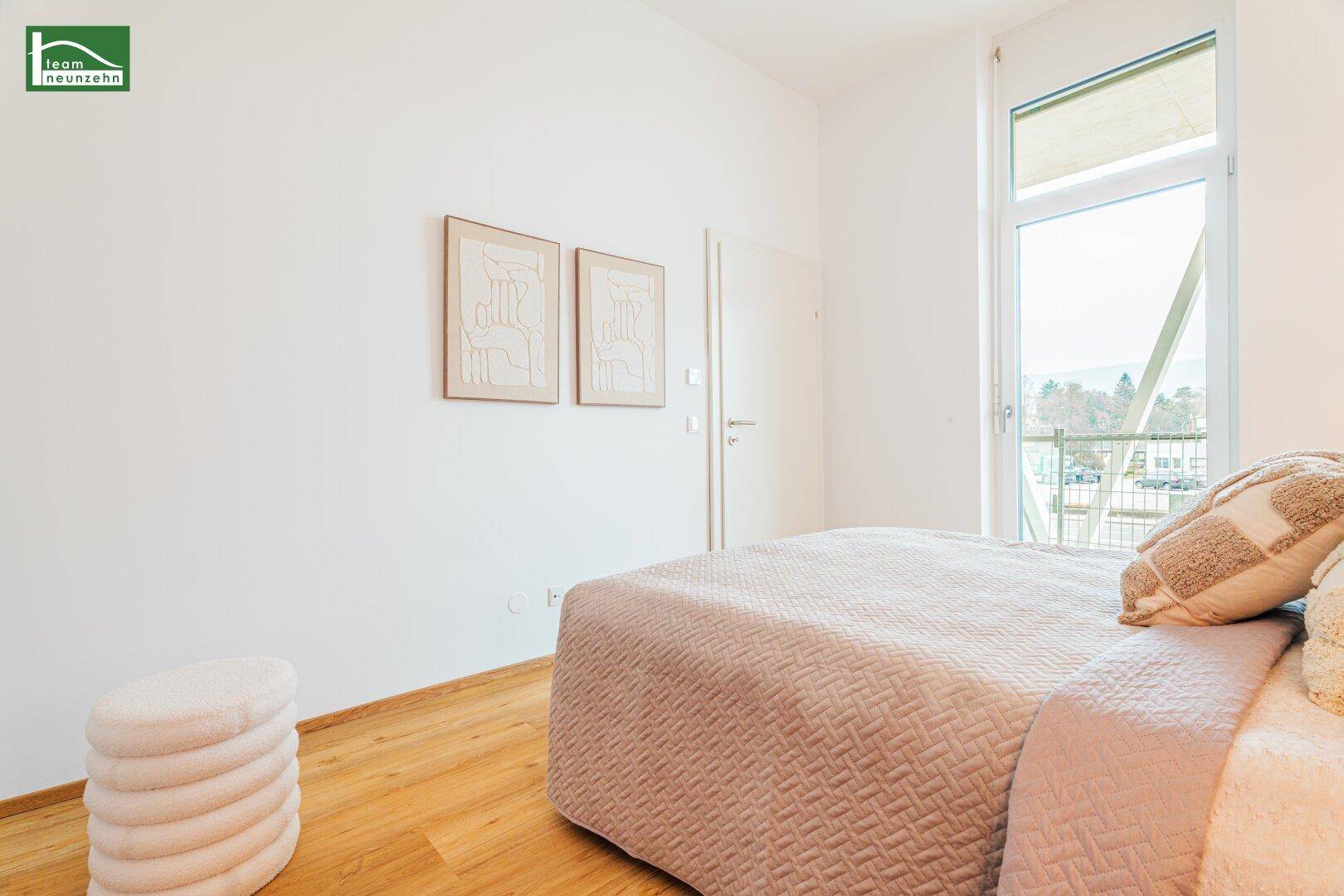 Helles Schlafzimmer mit Holzboden, großen Fenstern und Zugang zu einem Balkon.