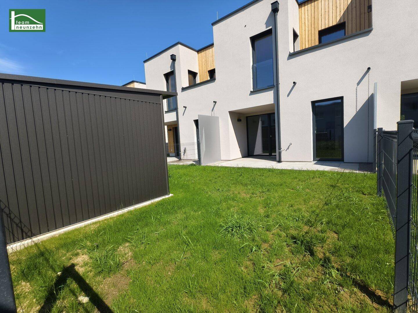 Gepflegter Gartenbereich mit Rasenfläche und Blick auf die moderne Reihenhausfassade unter blauem Himmel.