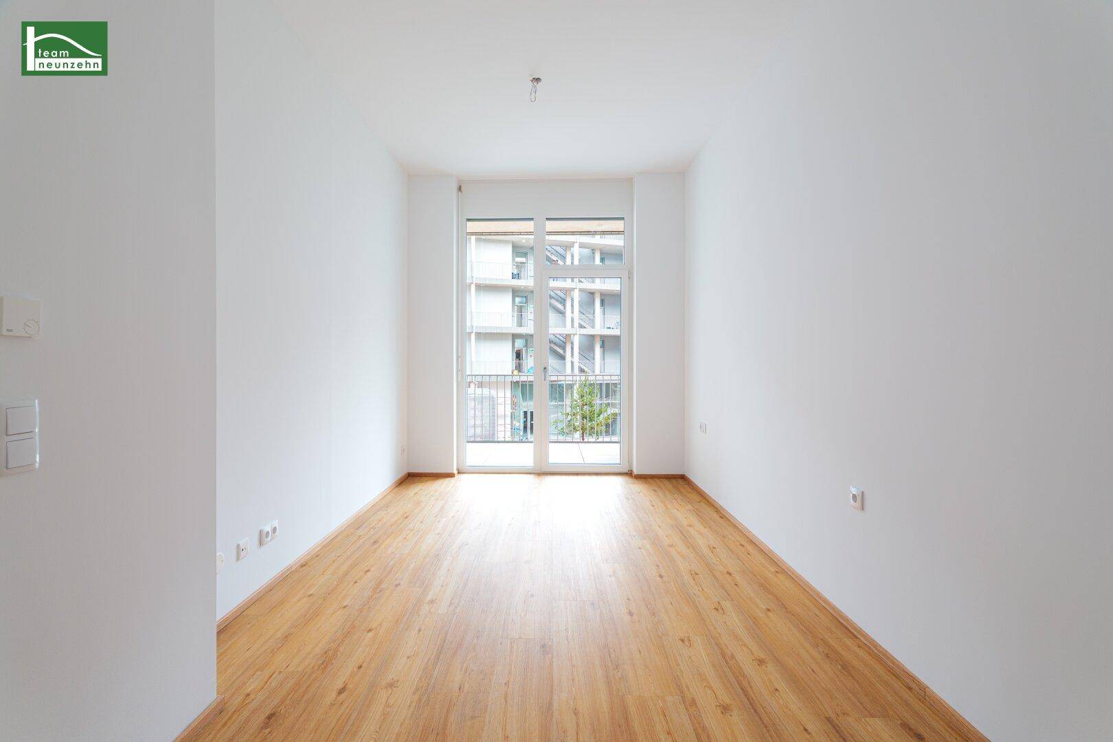 Helles, leeres Zimmer mit Holzboden und Zugang zu einem französischen Balkon.