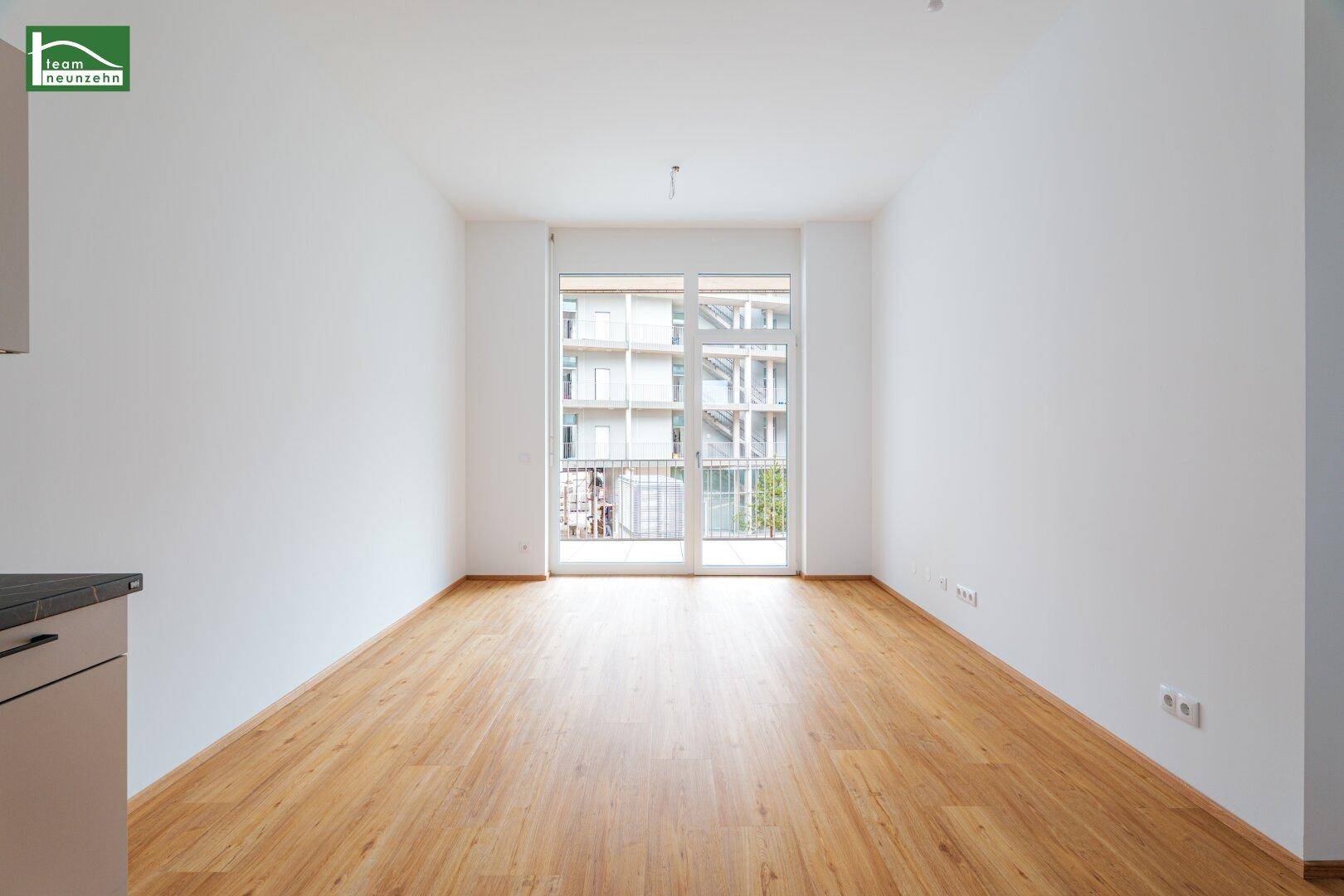 Leerer Wohnraum mit hellem Laminatboden und Zugang zu einem französischen Balkon.