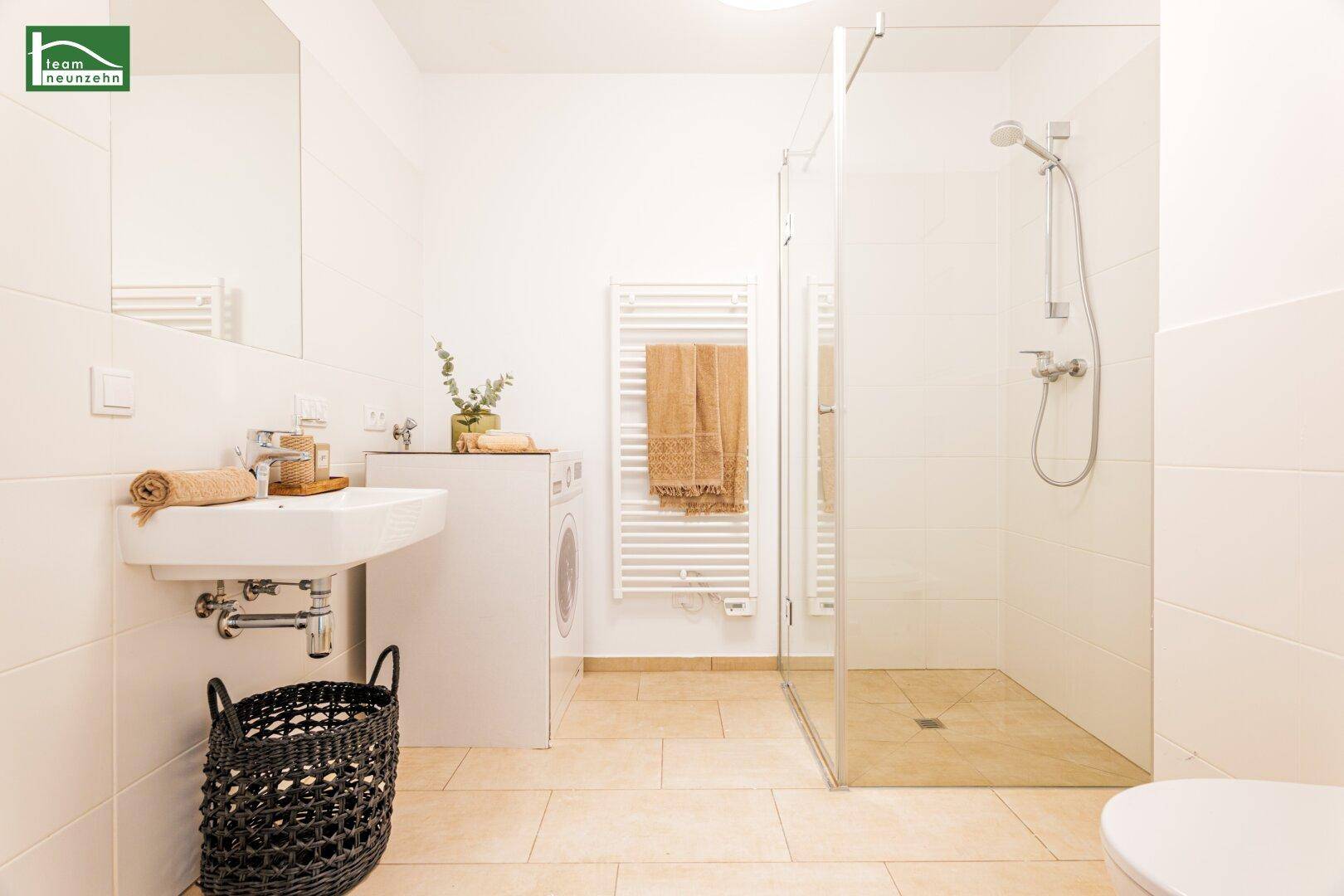 Modernes Badezimmer mit Dusche, Waschbecken, WC und Waschmaschine, hell gefliest.