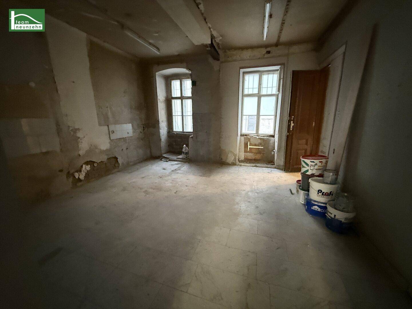 Unrenovierter Innenraum mit zwei großen Fenstern und sichtbaren Renovierungsspuren, bereit für die Neugestaltung.