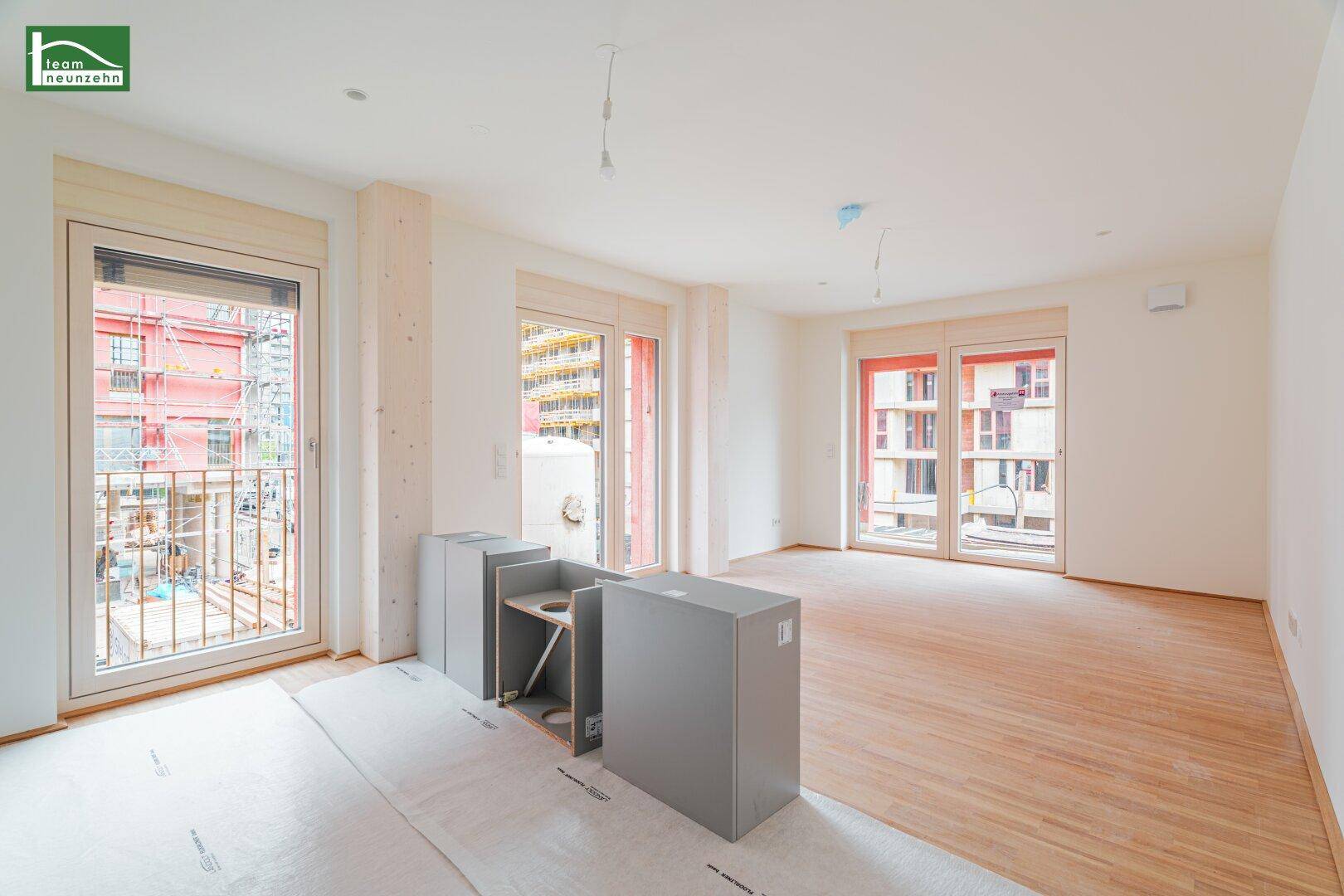 Heller Raum mit Holzboden und mehreren Balkonzugängen, vorbereitet für eine moderne Küche.