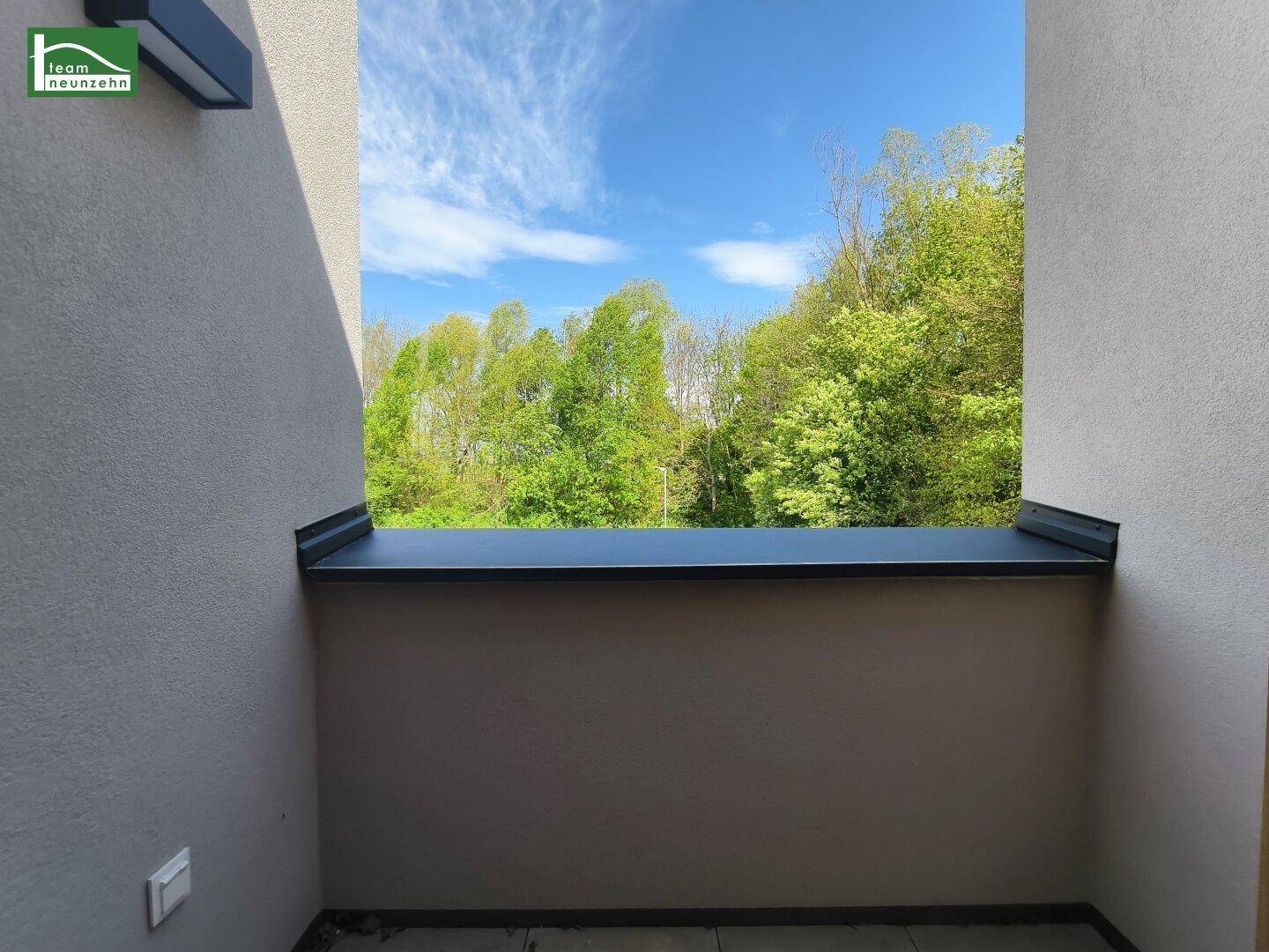 Überdachte Loggia mit Blick ins Grüne und hellem Putz an den Wänden.