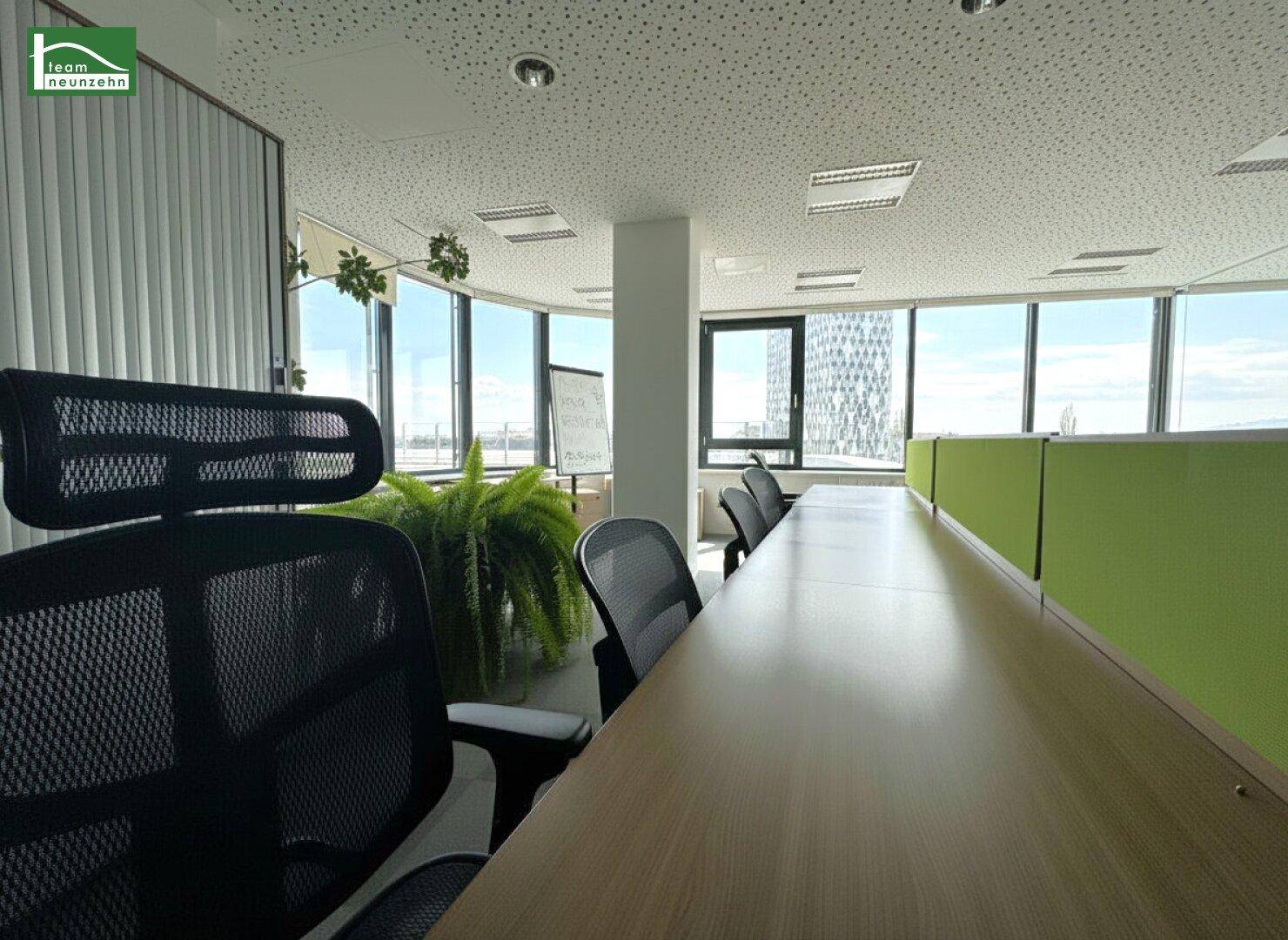 Offenes Büro mit mehreren Arbeitsplätzen, großen Fenstern und Blick auf die Stadt und die Umgebung.