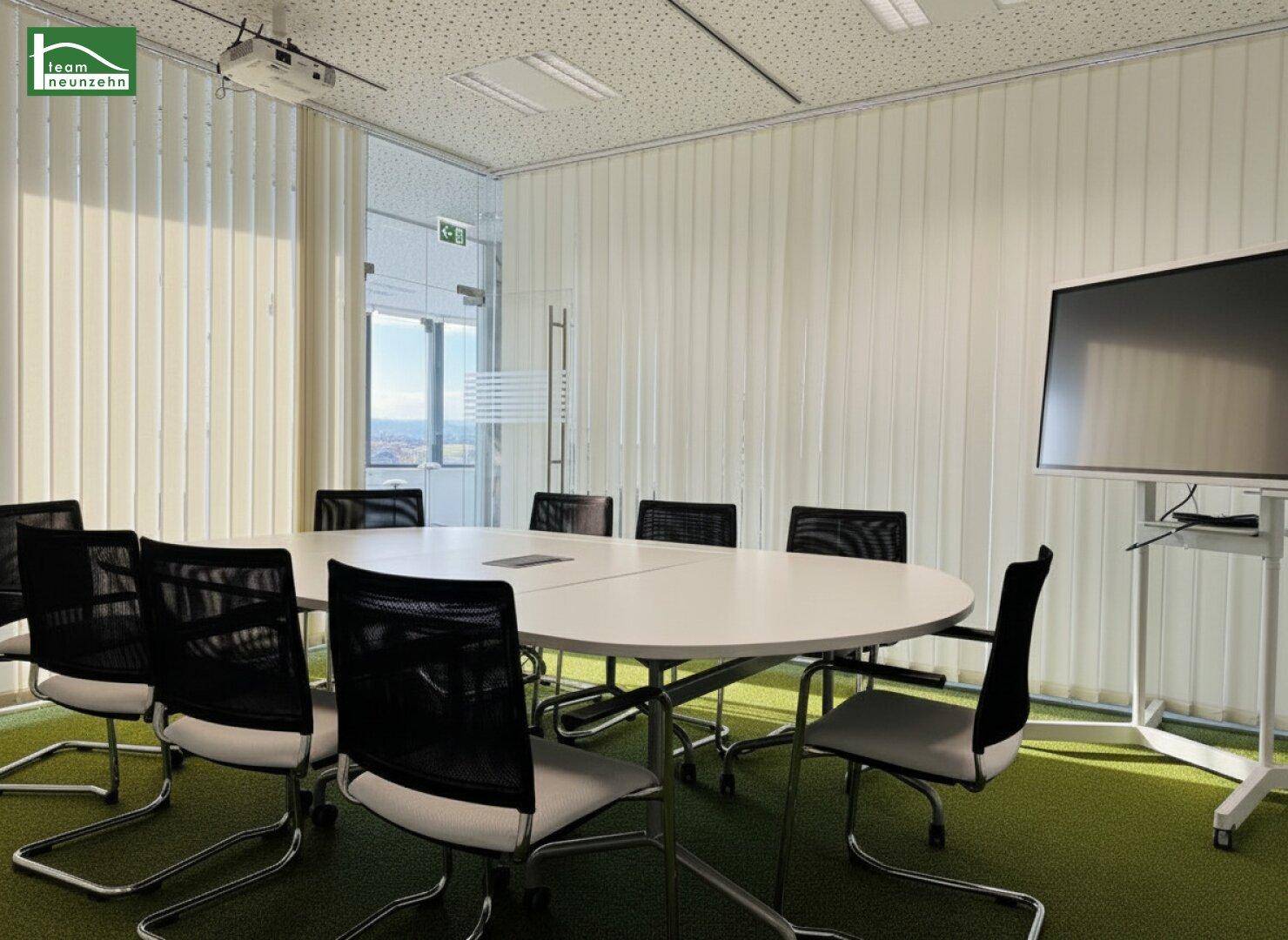 Moderner Konferenzraum mit ovalem Tisch, ergonomischen Stühlen und Blick auf die Stadt durch große Fenster.