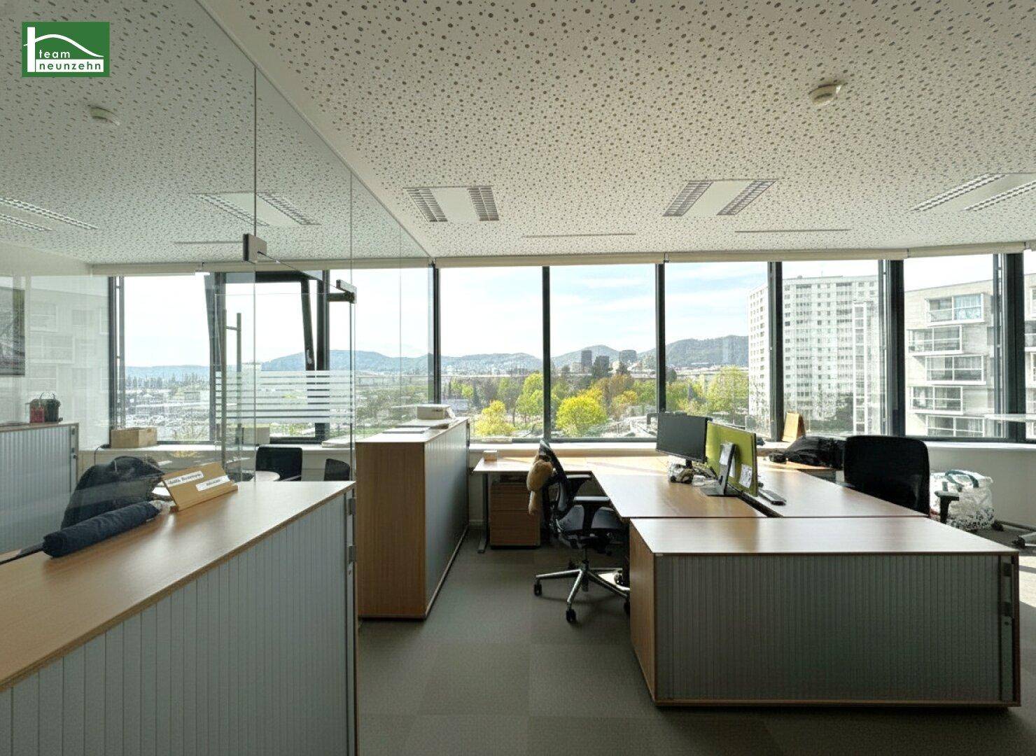 Großes Büro mit mehreren Arbeitsplätzen, Glaswänden und Panoramablick auf die Stadt und die Landschaft.