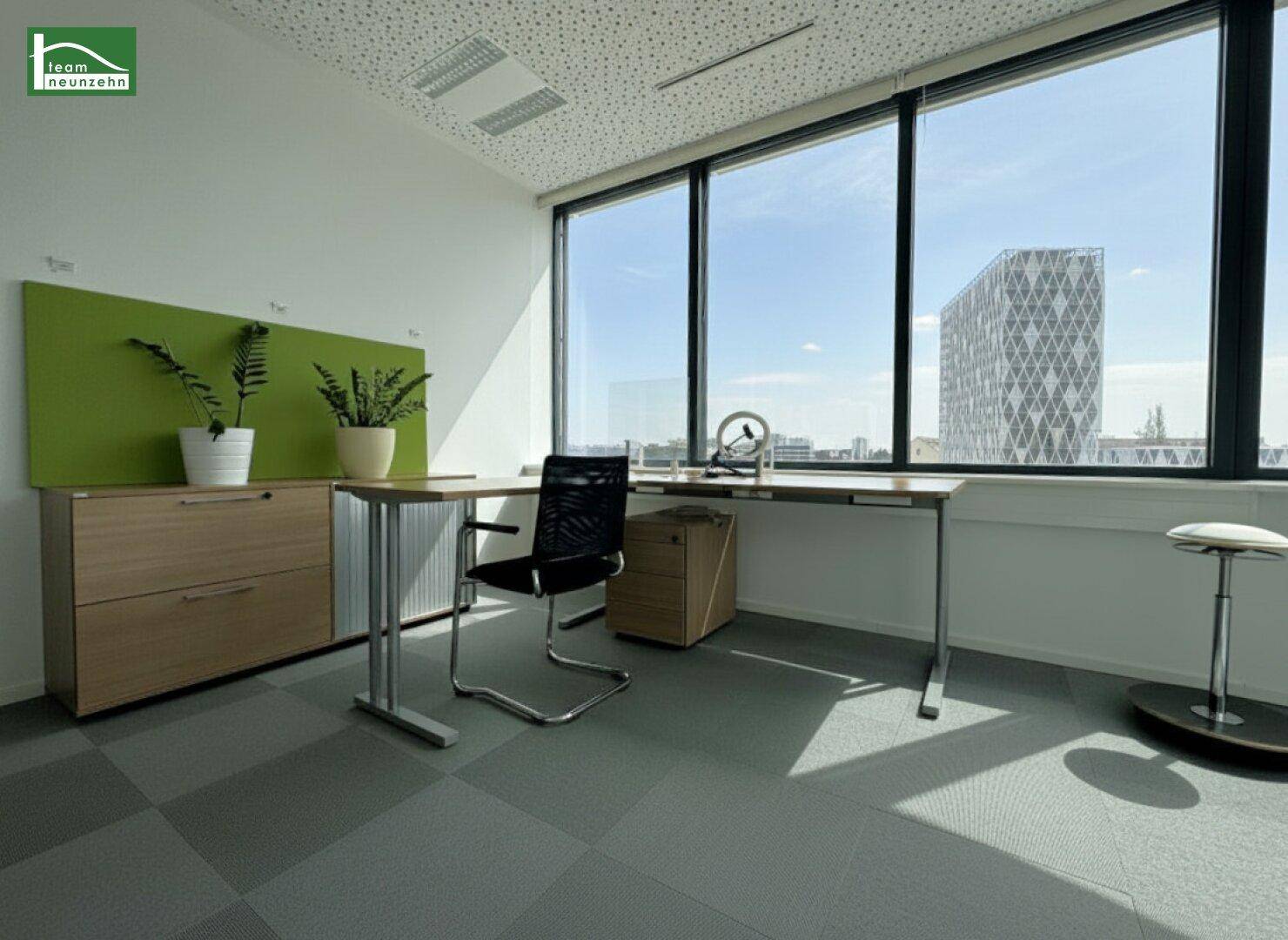 Helles Büro mit großen Fenstern, modernem Schreibtisch und Blick auf die Stadt und ein markantes Gebäude.