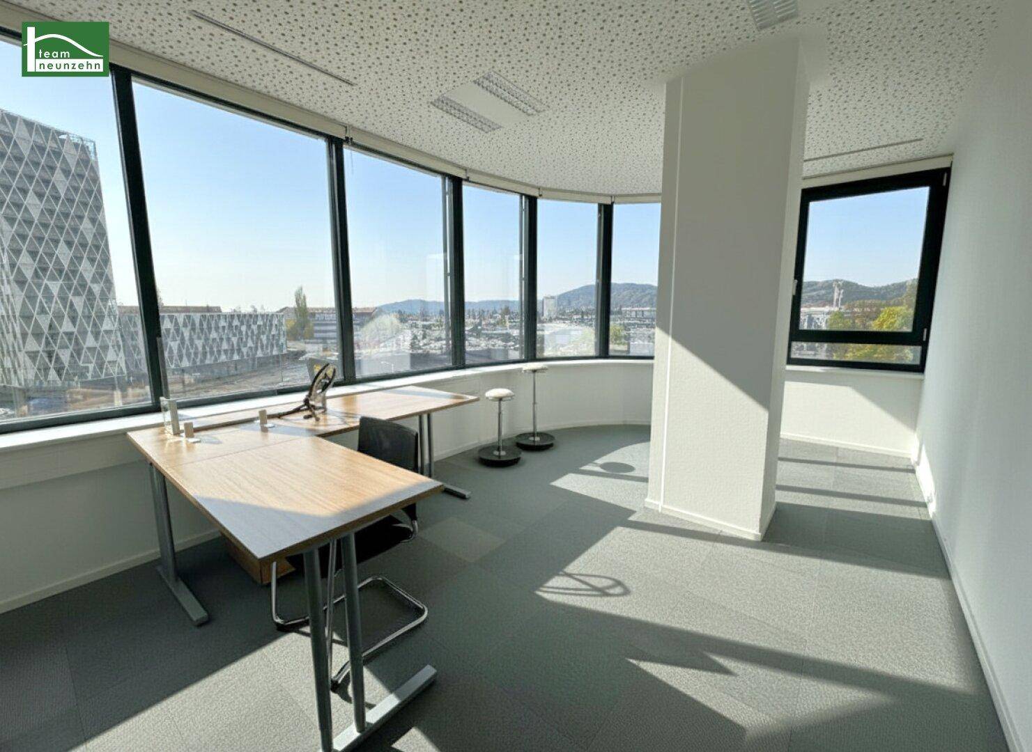 Helles Eckbüro mit geschwungenen Fenstern, die einen weiten Blick über die Stadt ermöglichen.