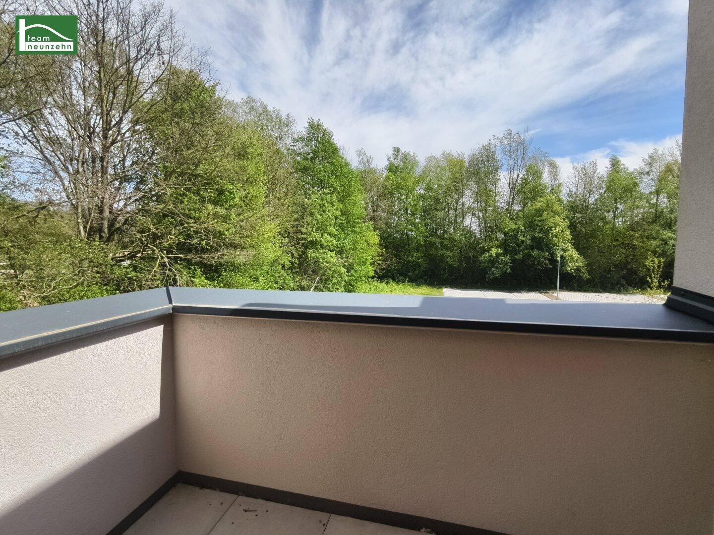 Balkon mit Fliesenboden und einem schönen Blick ins Grüne mit Bäumen.