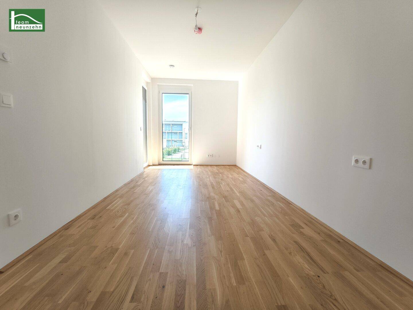 Helles, leeres Zimmer mit Parkettboden und Zugang zu einem Außenbereich.