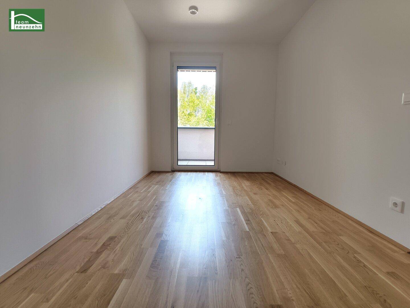 Helles Schlafzimmer mit Holzboden und Fenster mit Blick auf Bäume, bereit zur Einrichtung.