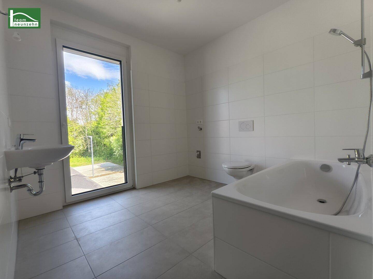 Modernes Badezimmer mit Badewanne, Waschbecken und Fenster mit direktem Zugang zum Garten.