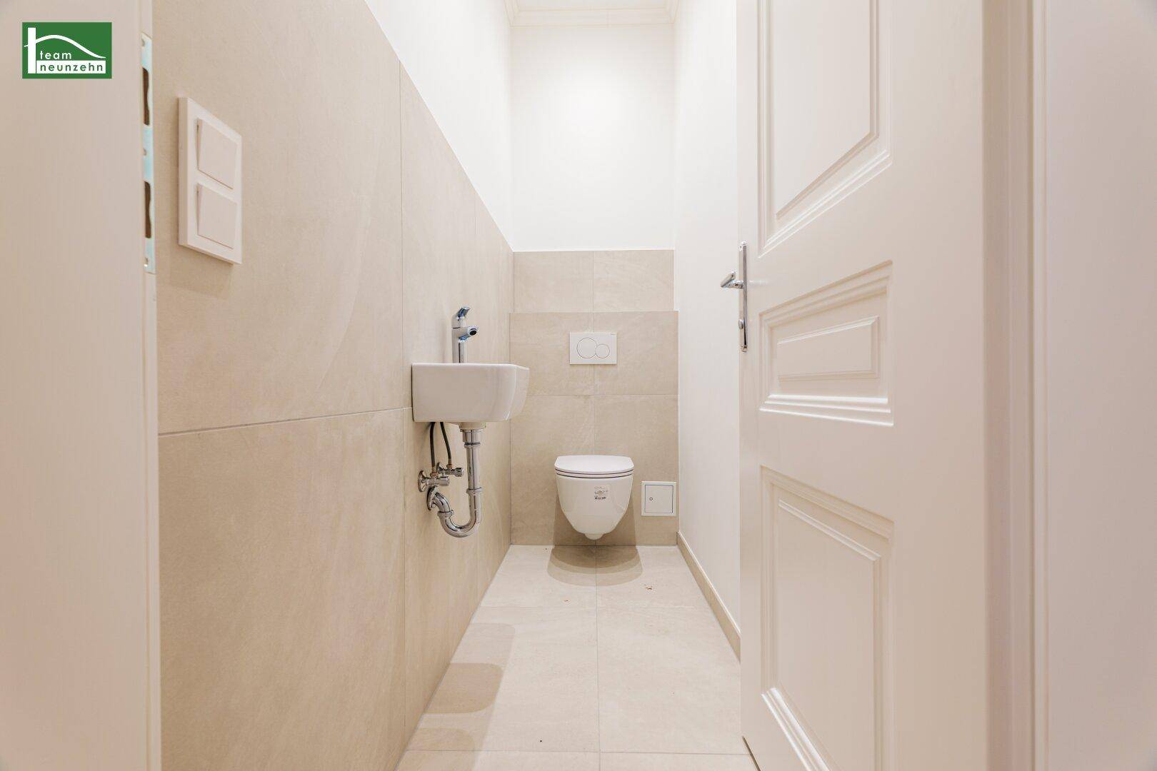 Modernes Gäste-WC mit beigefarbenen Fliesen, wandhängendem WC und kleinem Waschbecken.