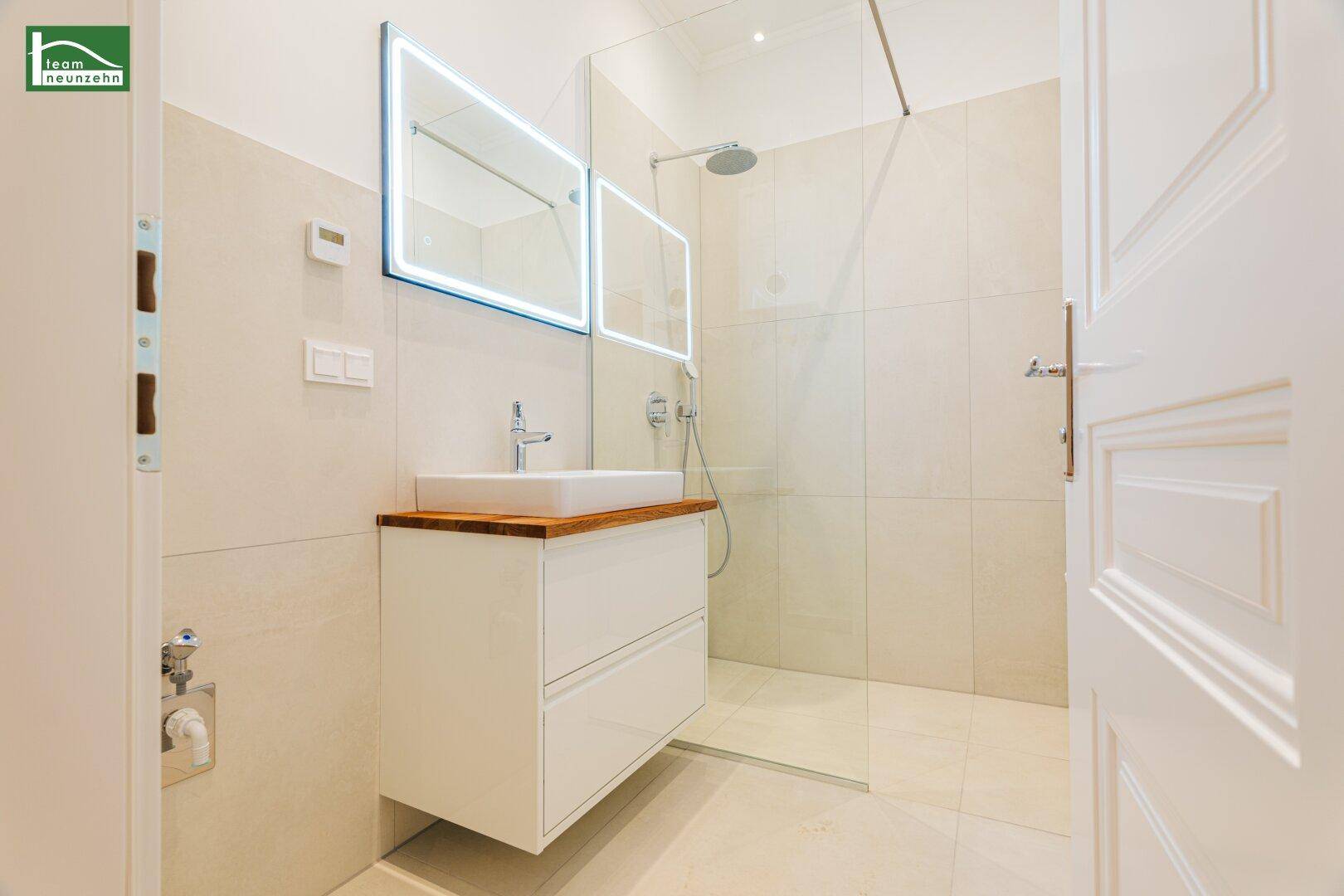 Modernes Badezimmer mit beigefarbenen Fliesen, Waschtisch und großer begehbarer Dusche.