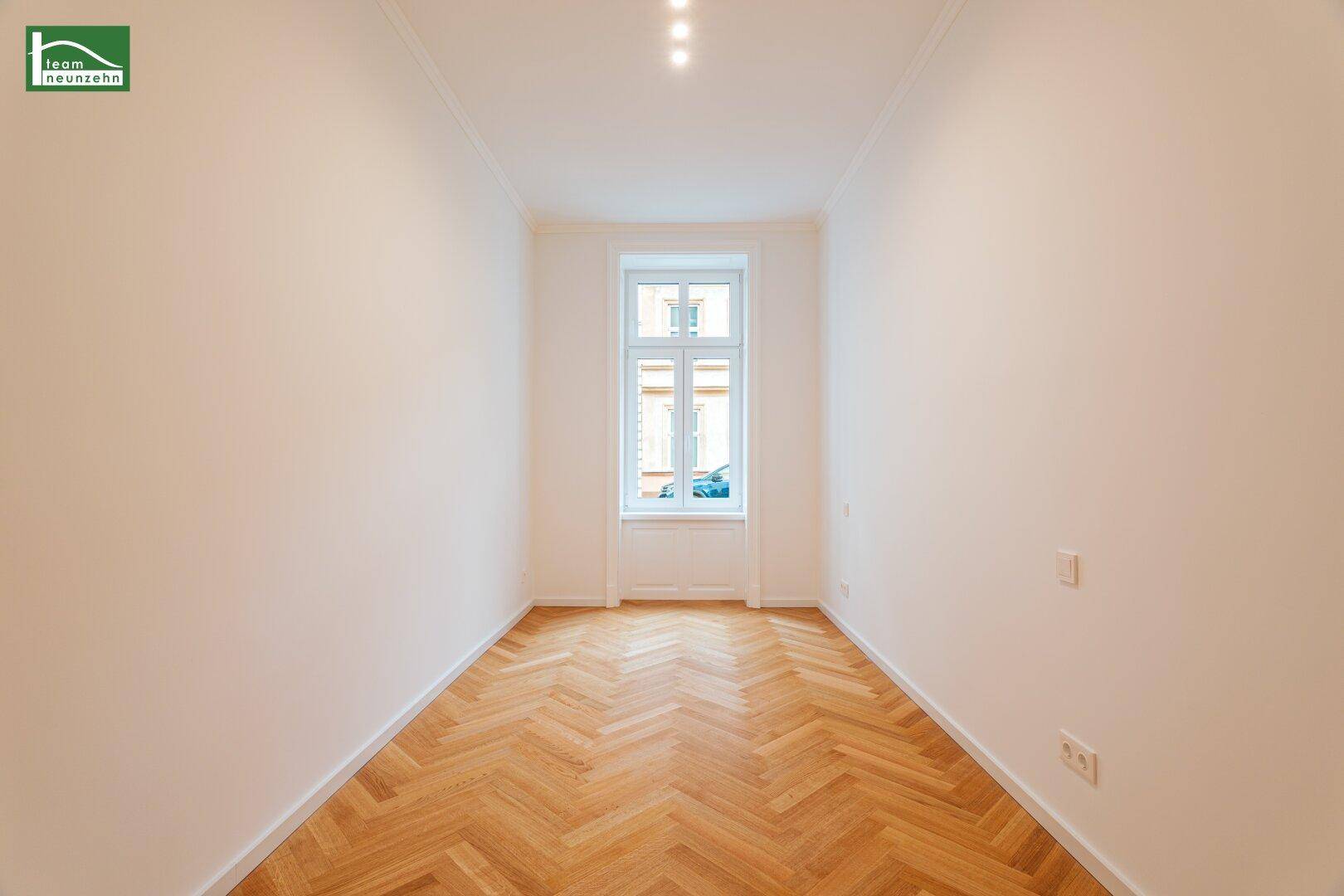 Schmaler Raum mit Fischgrätparkettboden, weißen Wänden und einem Fenster.