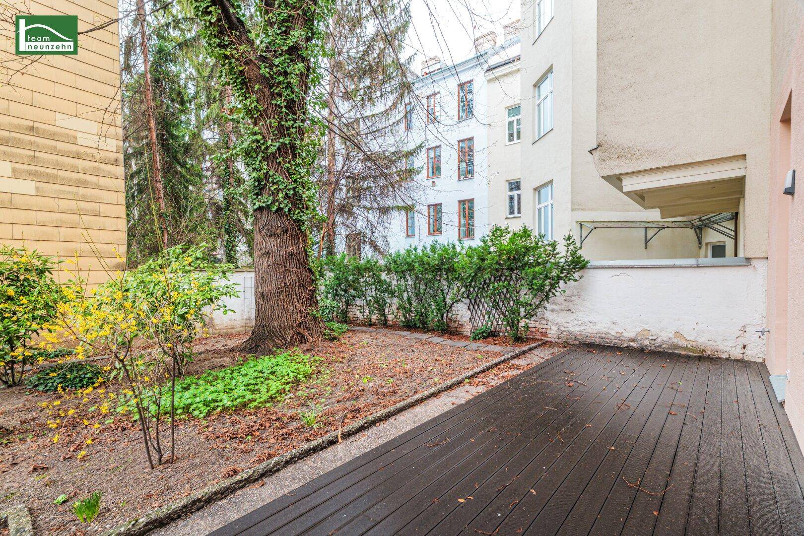 Terrasse mit Holzbelag und angrenzendem Gartenbereich mit Sträuchern und Bäumen.