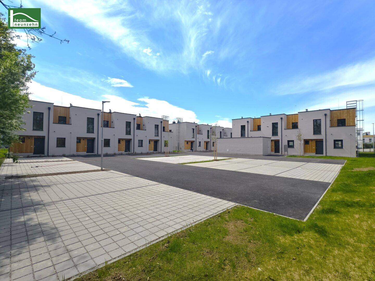 Reihe moderner Reihenhäuser mit Parkplätzen und Grünflächen in einer Neubausiedlung.