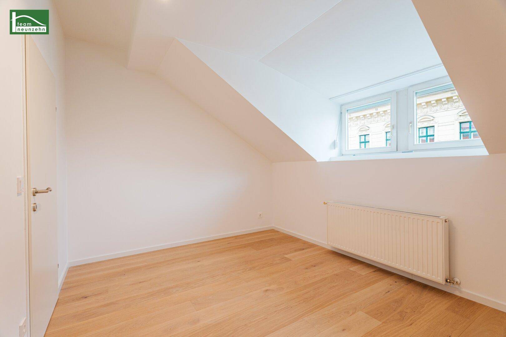 Helles Schlafzimmer im Dachgeschoss mit Parkettboden, Dachschräge und Fenster mit Stadtblick.