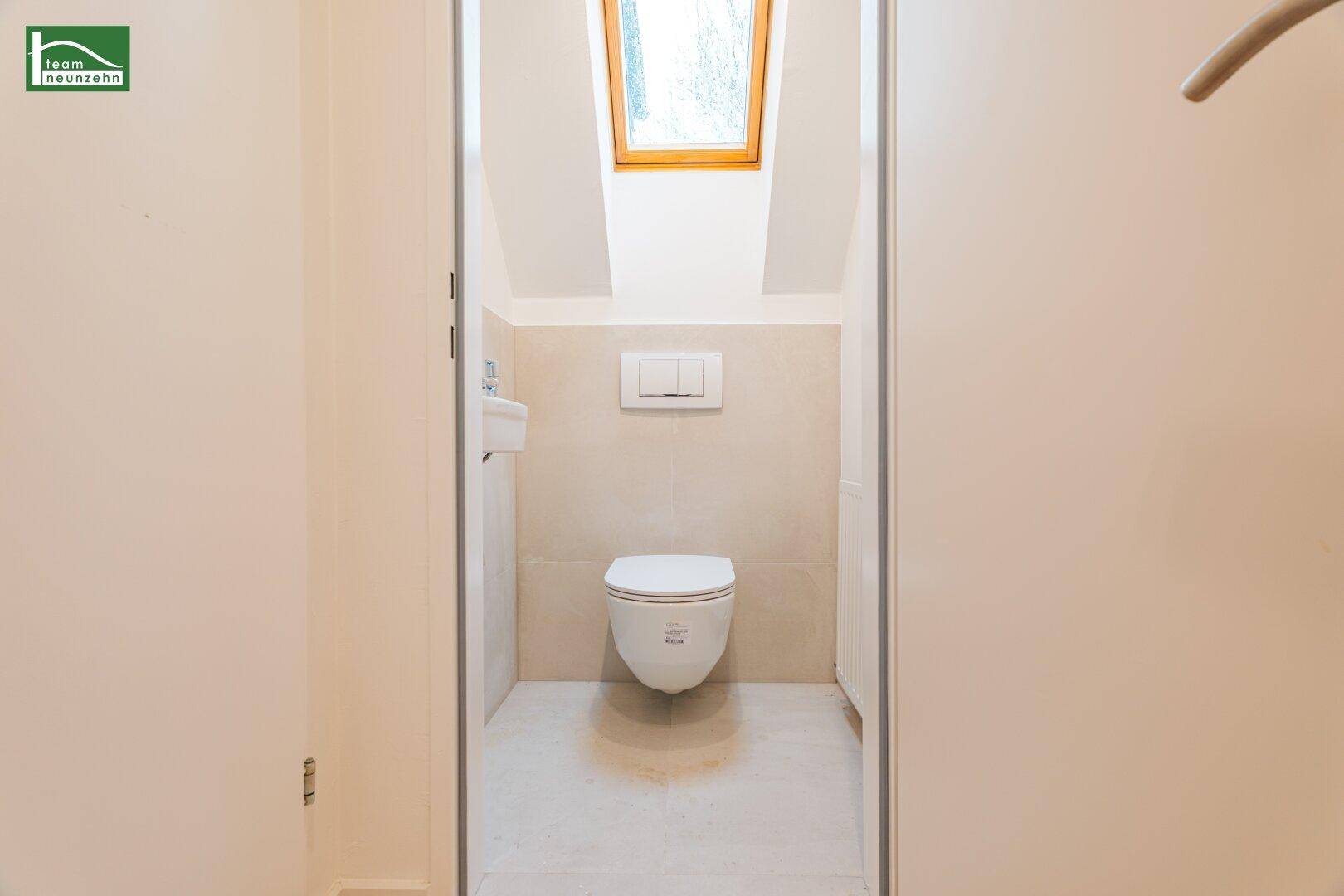 Modernes Gäste-WC mit Wand-WC, kleinem Waschbecken und Dachfenster für natürliche Belüftung.