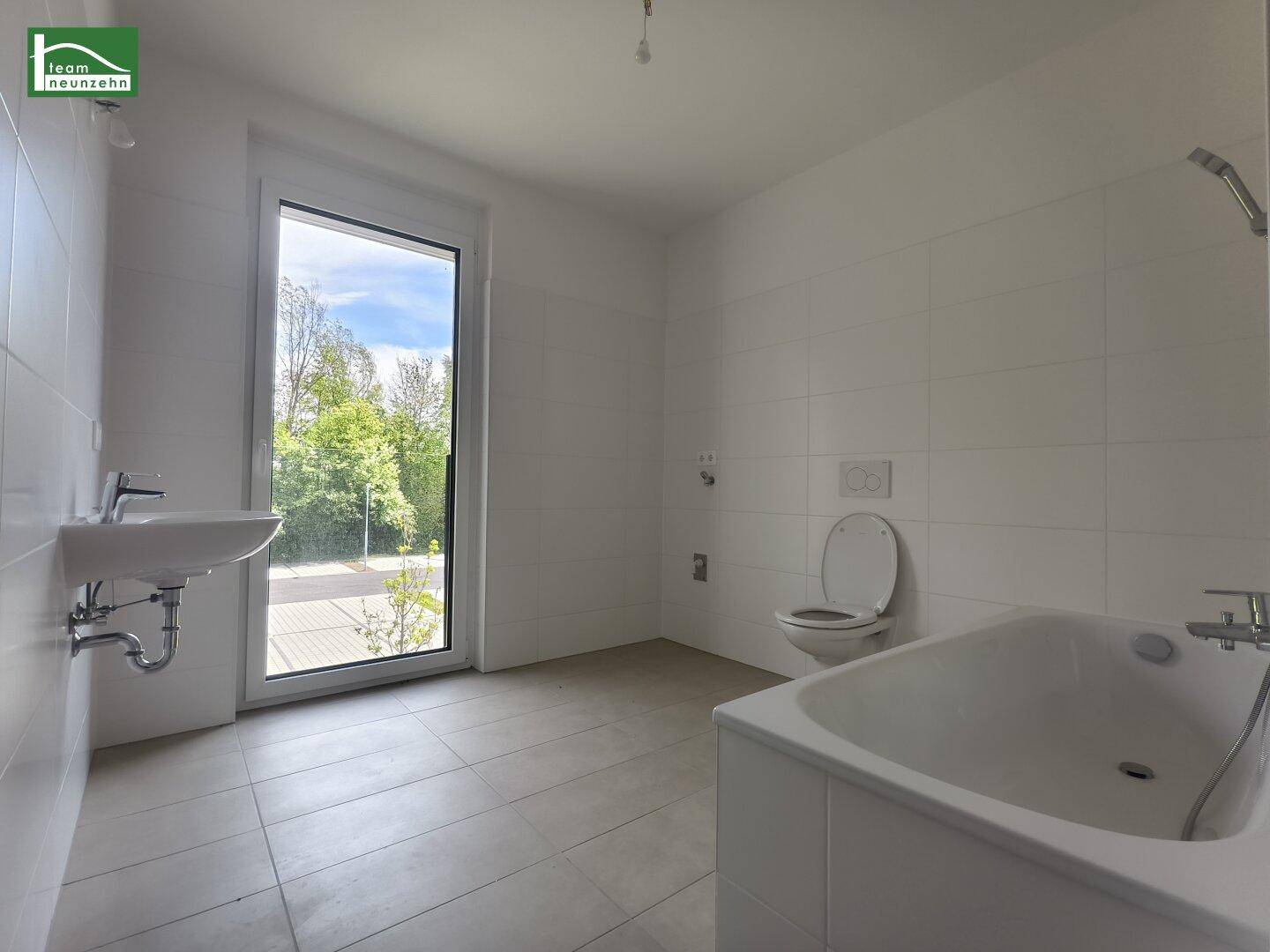 Modernes Badezimmer mit Badewanne, Waschbecken und großem Fenster für Tageslicht.