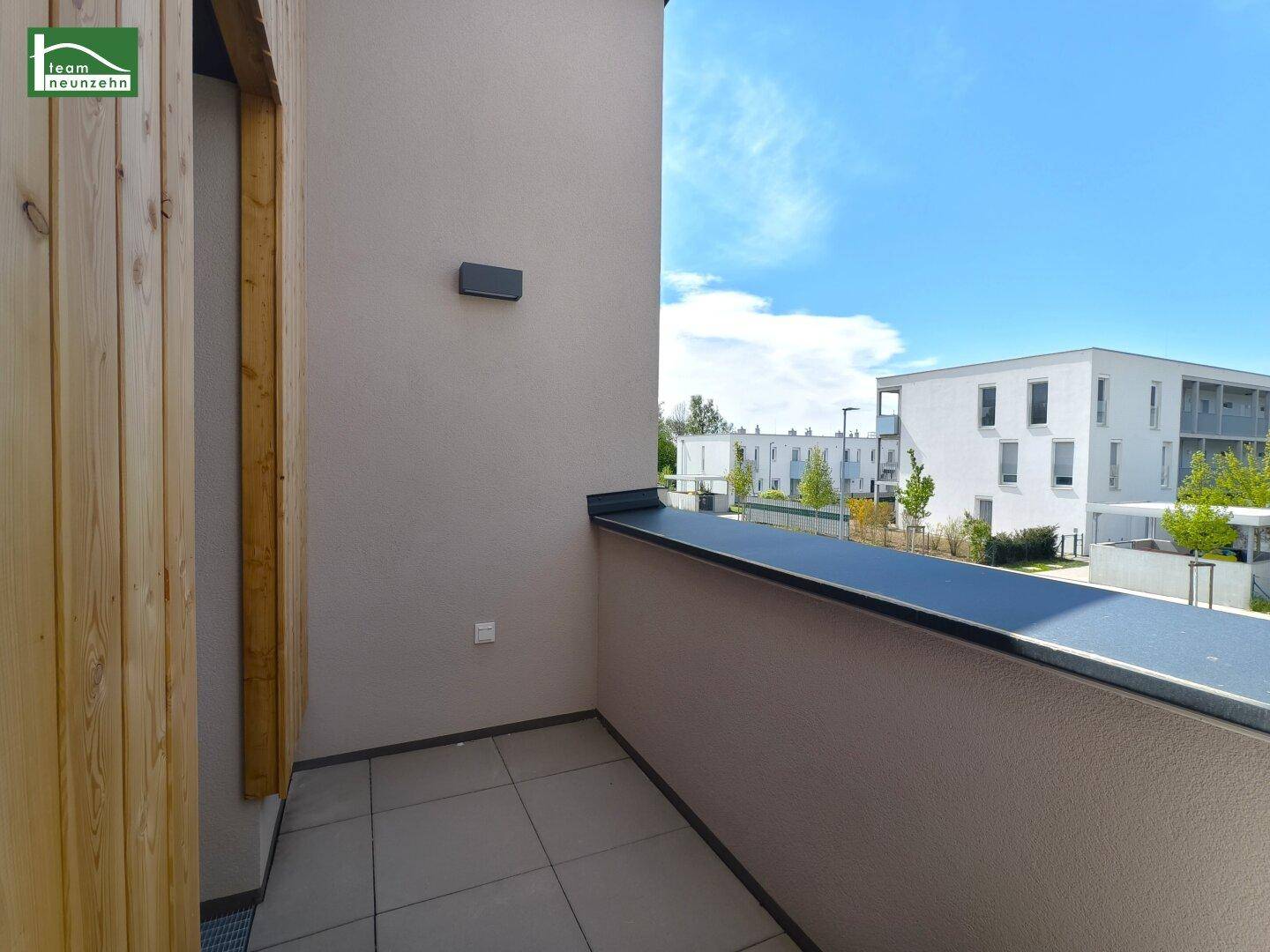 Kleiner Balkon mit Fliesenboden und Blick auf die umliegenden Neubauten.