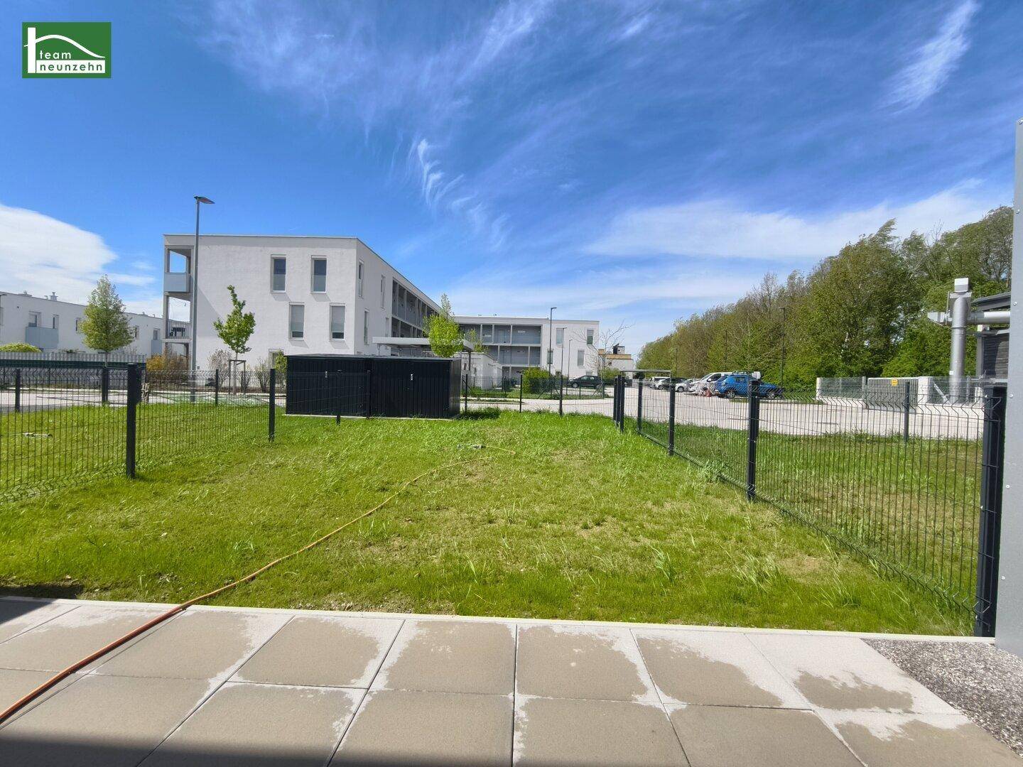 Moderner Neubau mit Rasenfläche und Parkplätzen unter blauem Himmel.