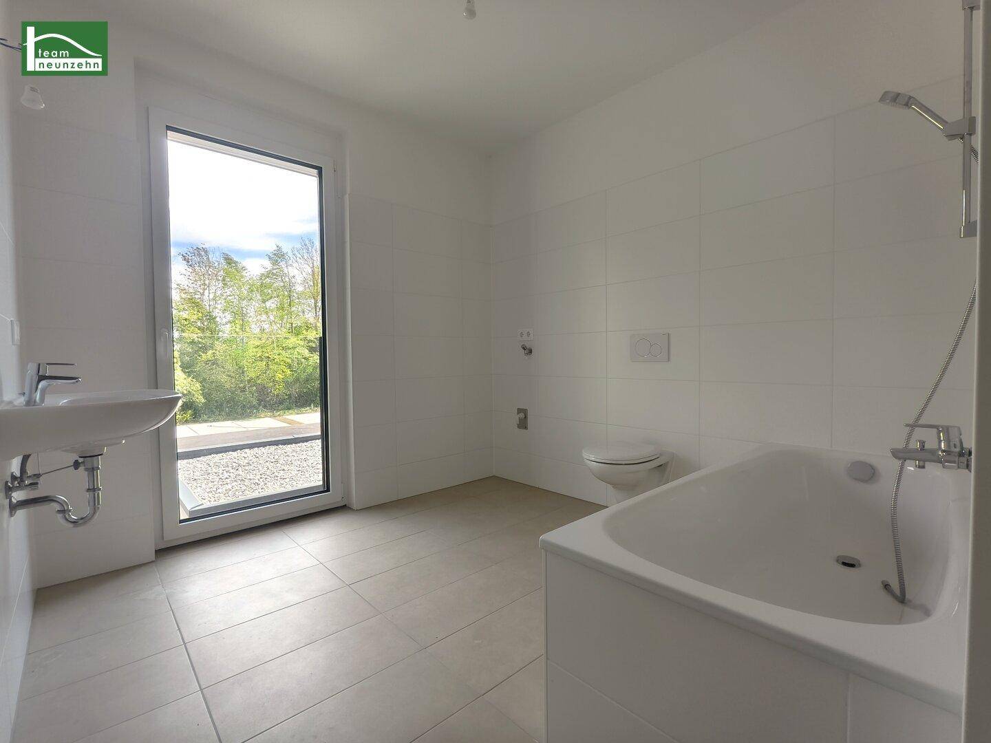 Helles Badezimmer mit Badewanne, WC und Fenster mit Blick ins Grüne.