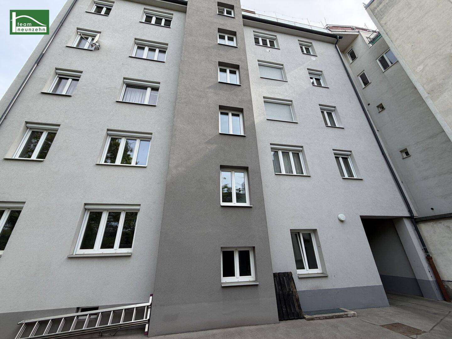 Rückseite eines Wohngebäudes mit vielen Fenstern und einem Durchgang zum Innenhof.